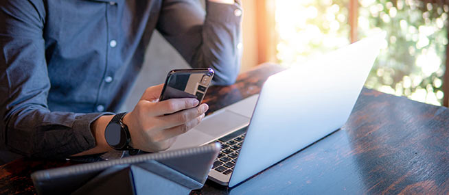 man-holding-phone-with-laptop-IS-1130938108