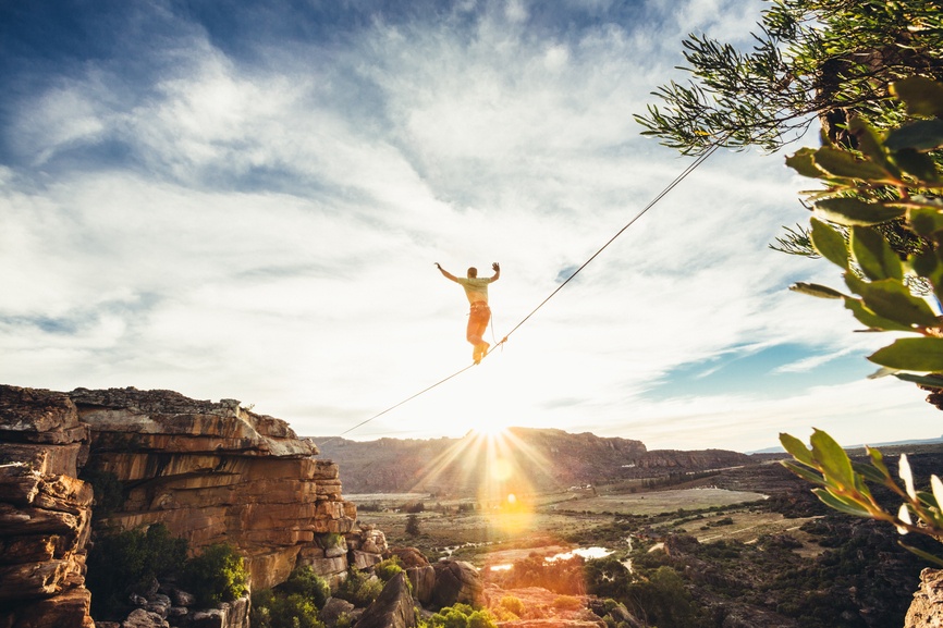 A man on a tightrope, halfway through his journey over a valley, symbolizes the risk of NNN investing.