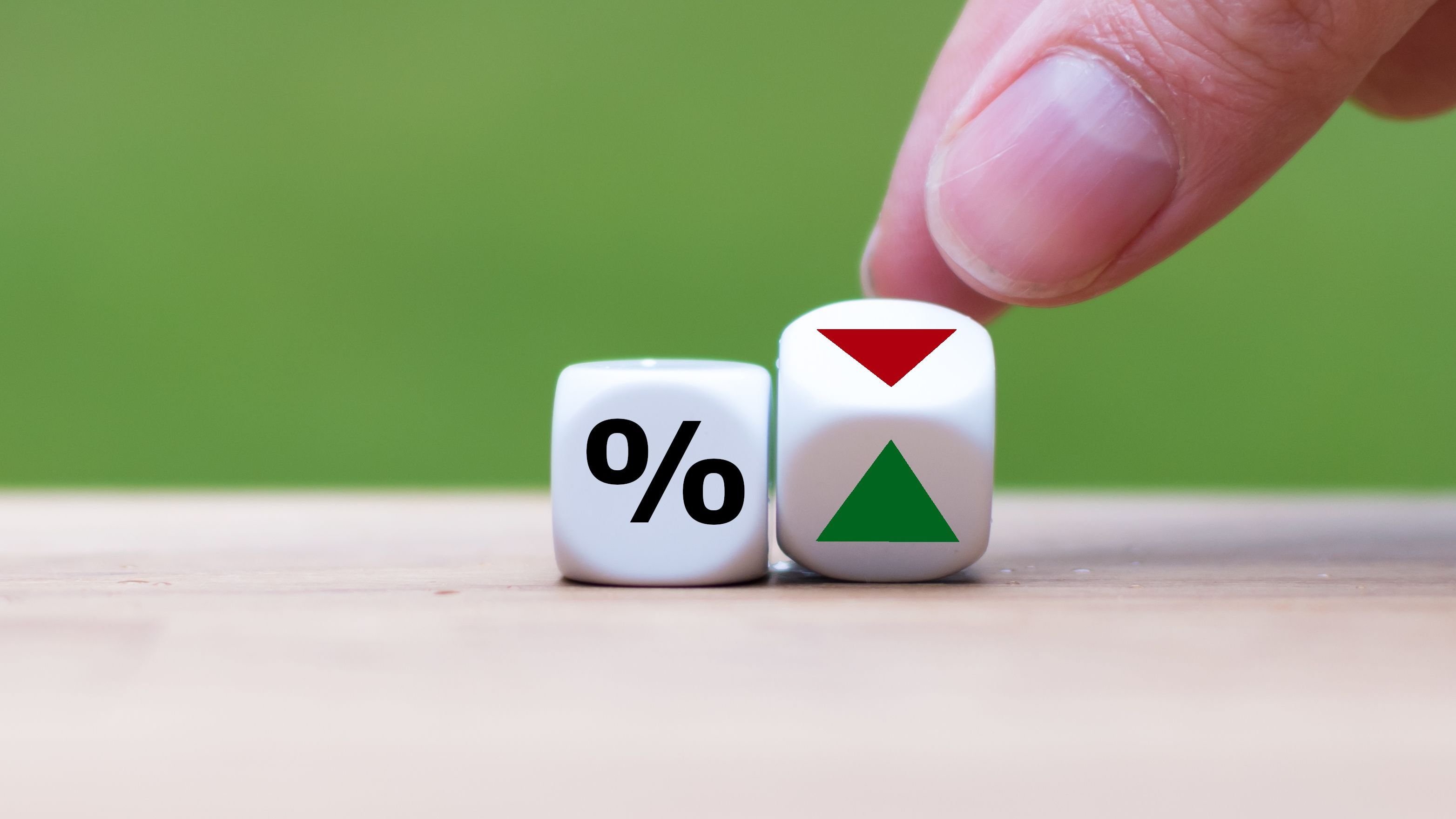 Hand is turning a dice and changes the direction of an arrow symbolizing that the interest rates are going down.