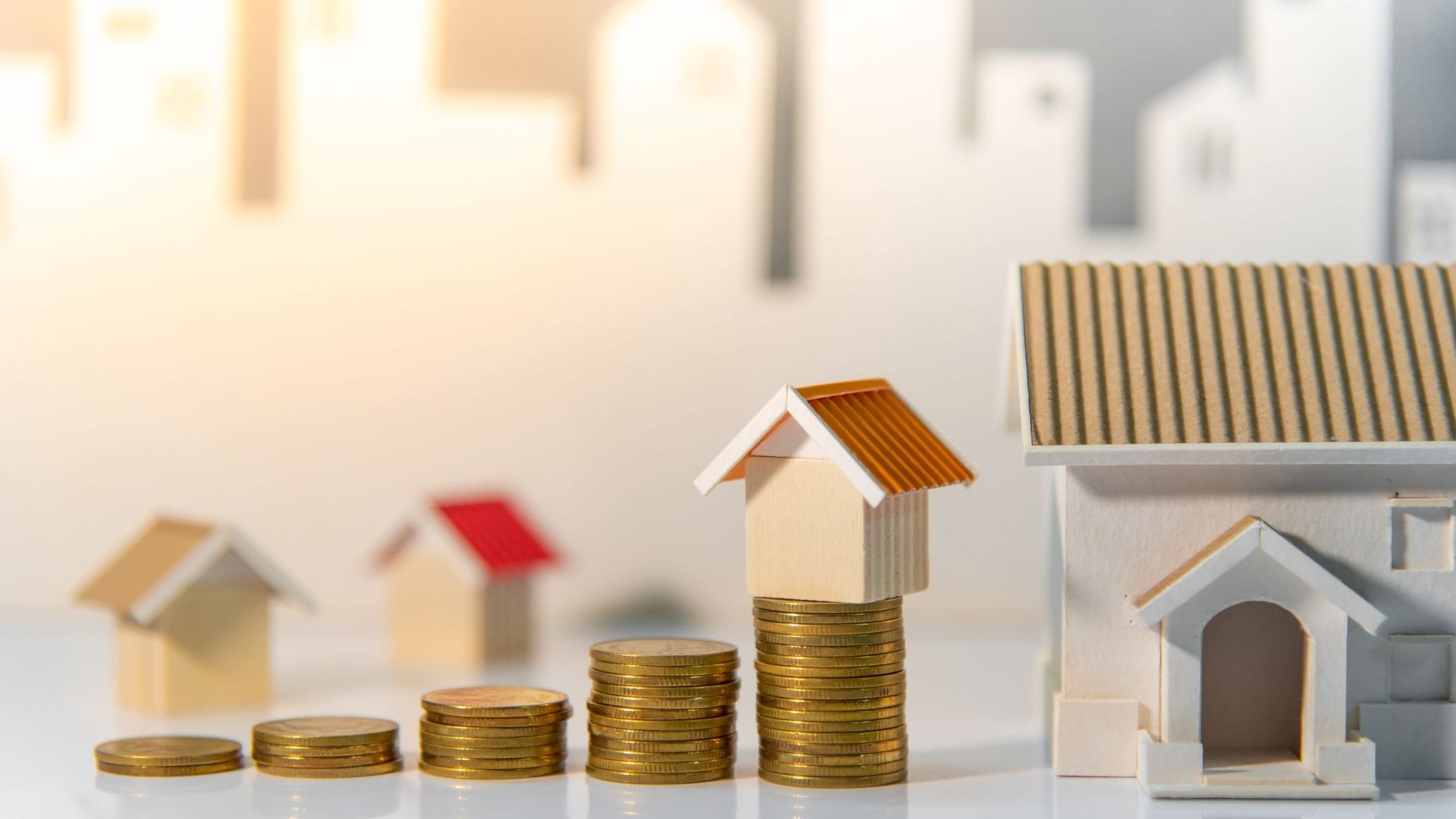 Coins stack and house model on the table with white city background. 