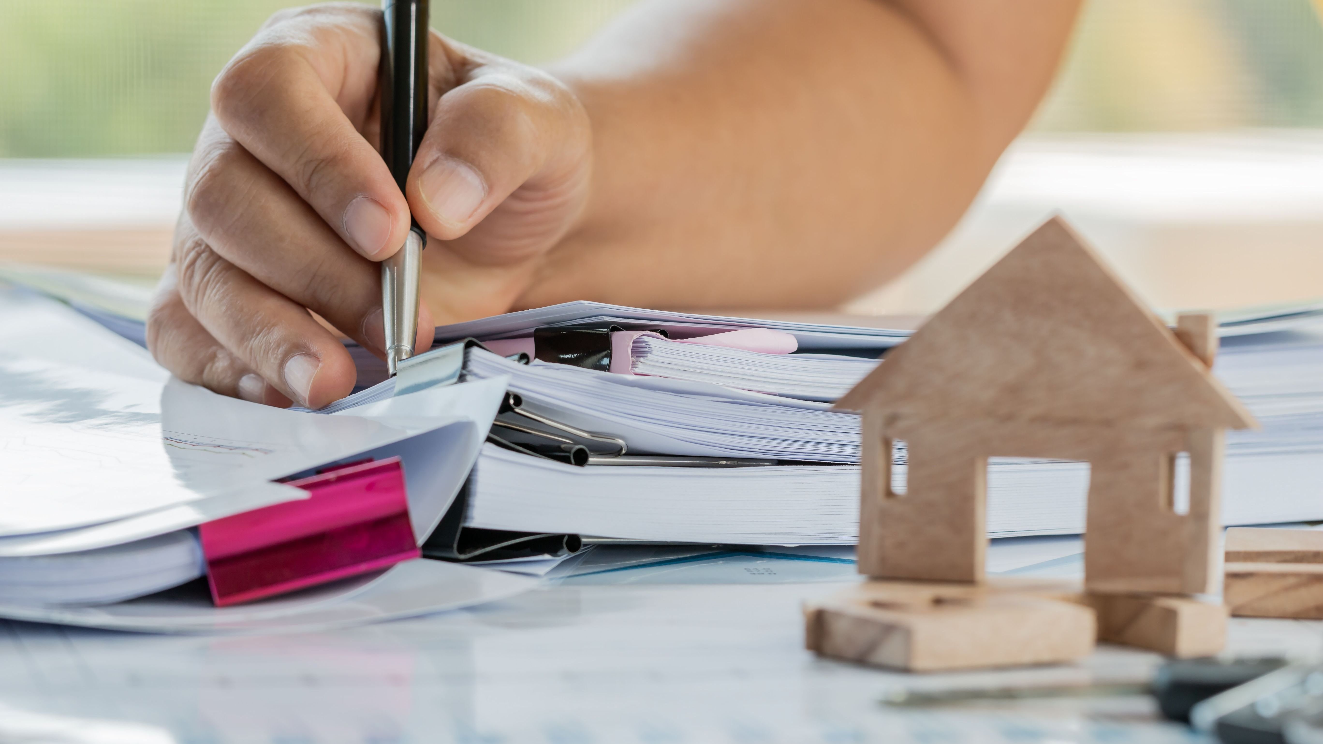 Businessman hands signing documents file paperwork financial market or property mortgage real estate investment business on work busy desk office with miniature wooden house models.