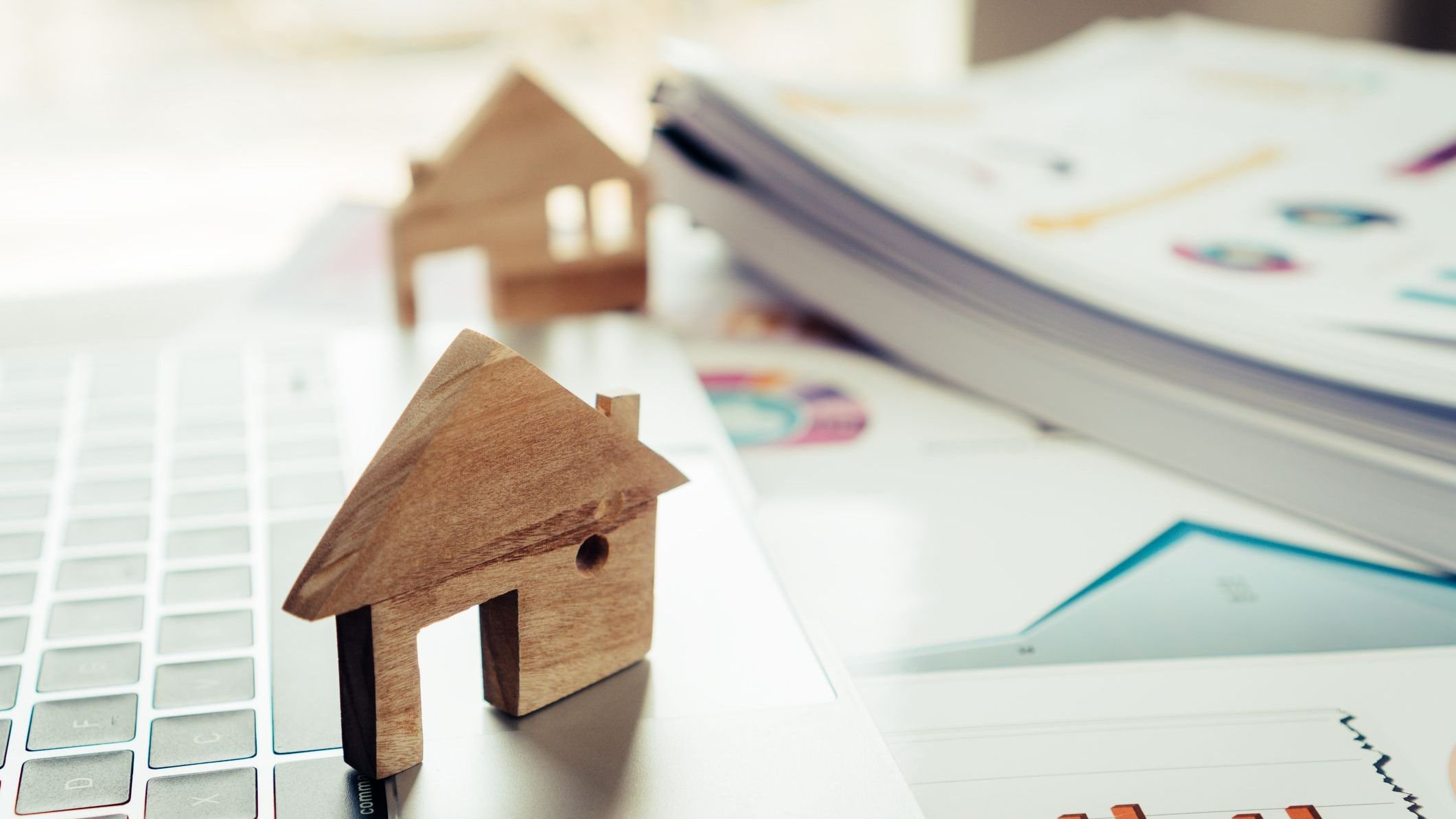 Wooden home model on computer with chart report documents.