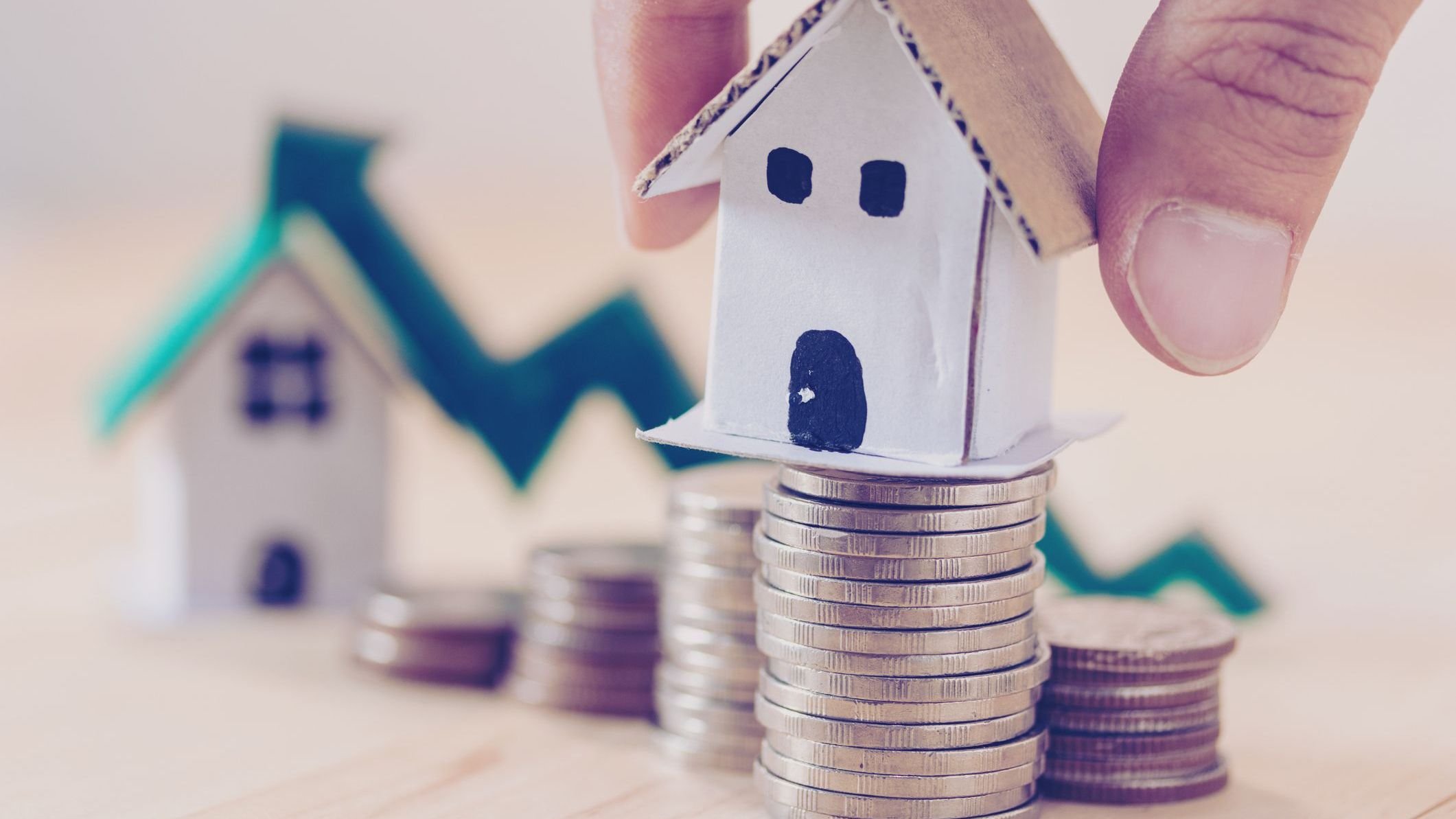 Wooden house model on stack of coins with upwards arrow in background.