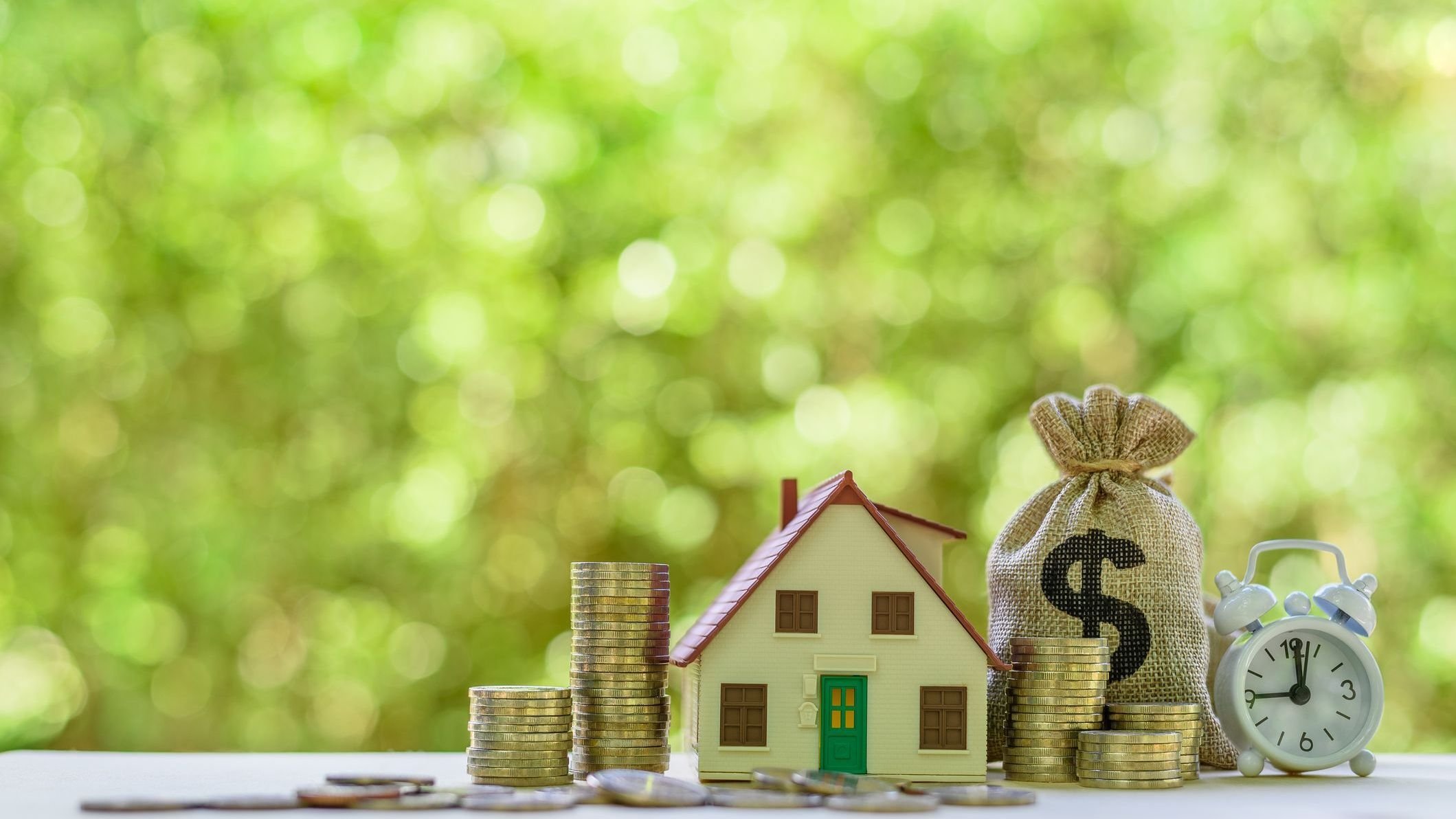 House model, coins, US dollar bag, white clock on a table.