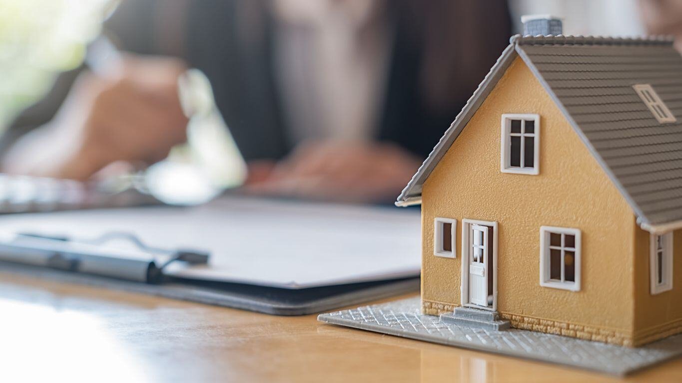 Little wooden house and papers sitting on a desk.