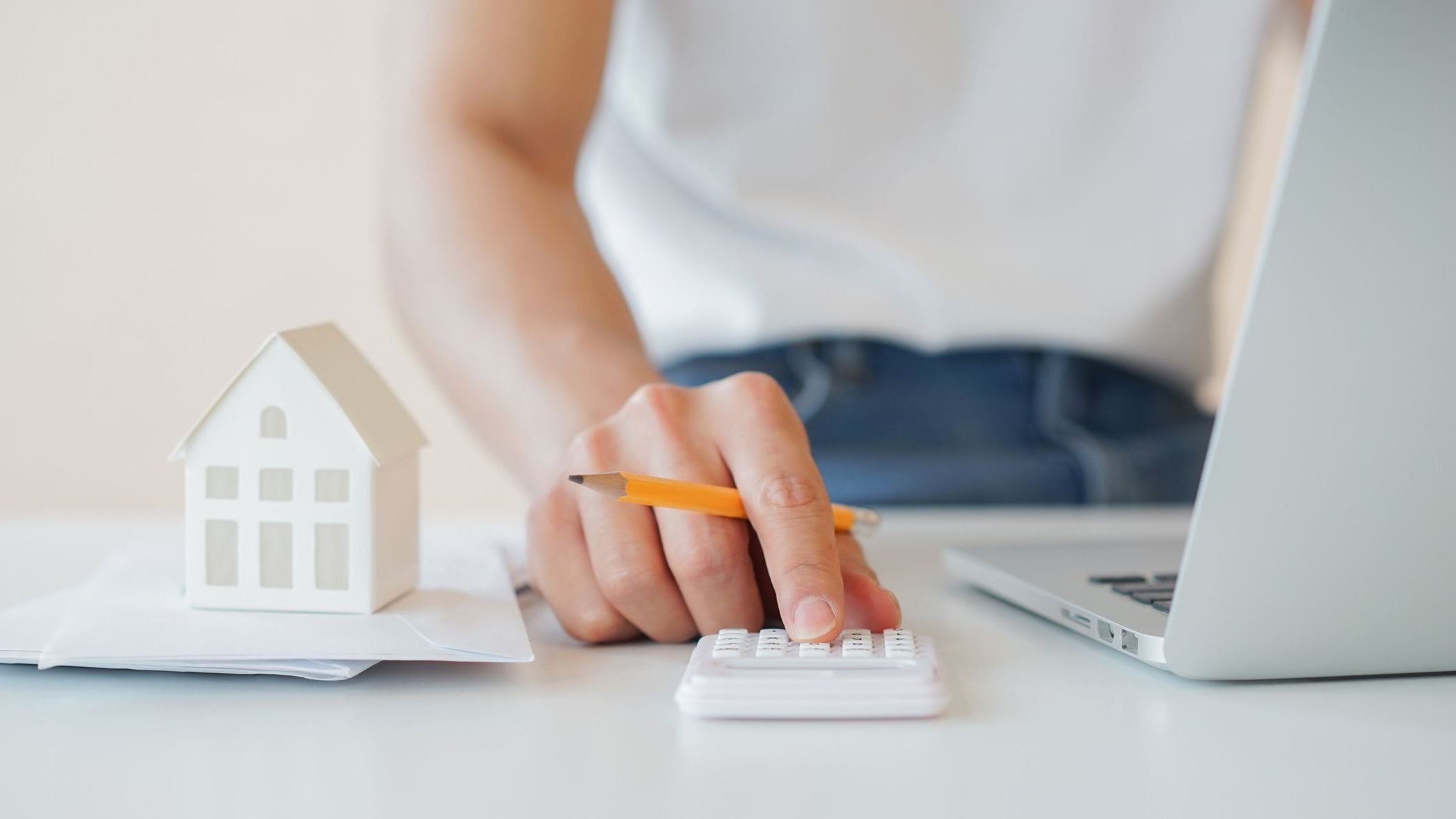 Close up man hand counting on calculator with house's model on invoice letter to summary of refinance expense for planning and manage money about home loan mortgage and interest rates for people lifestyle concept