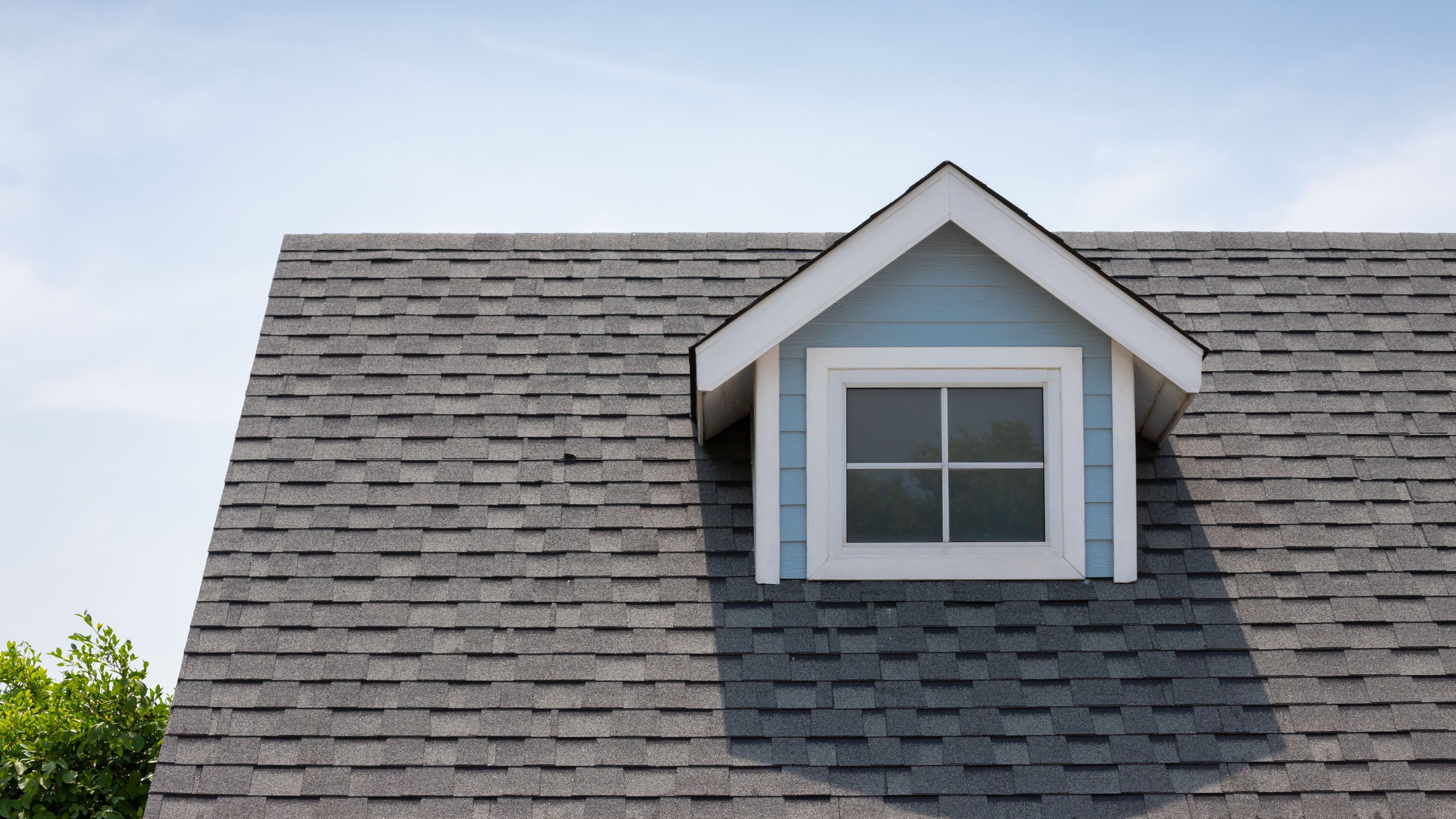 Search by image or video Roof shingles with garret house on top of the house among a lot of trees. dark asphalt tiles on the roof.