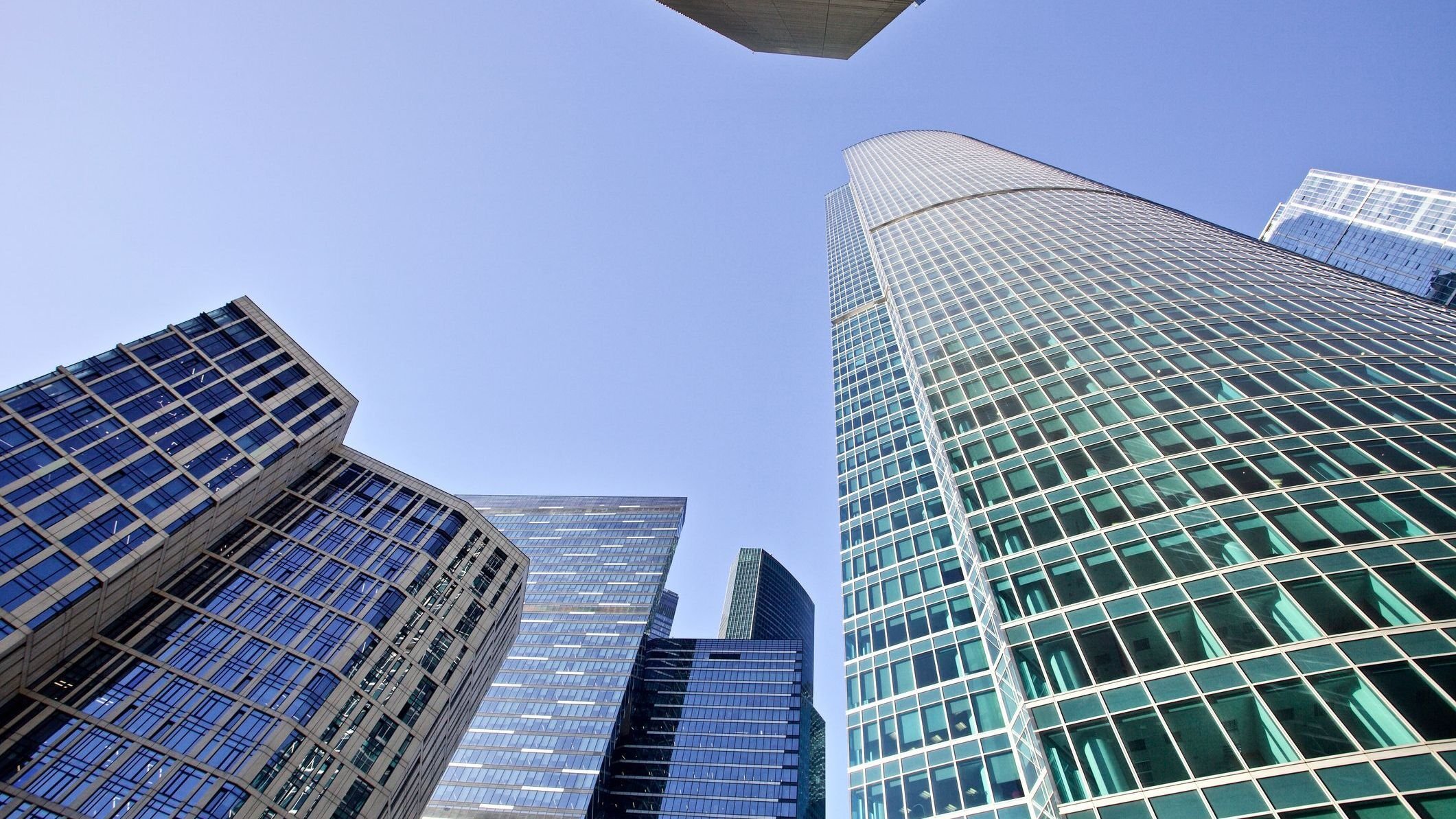 Bottom-up view of modern office buildings on bright clear blue sky.