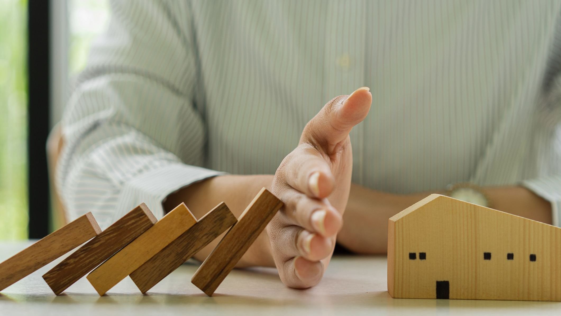 Businessman's risk investment protects the wooden block from falling wooden block dominoes on the desk in the office.