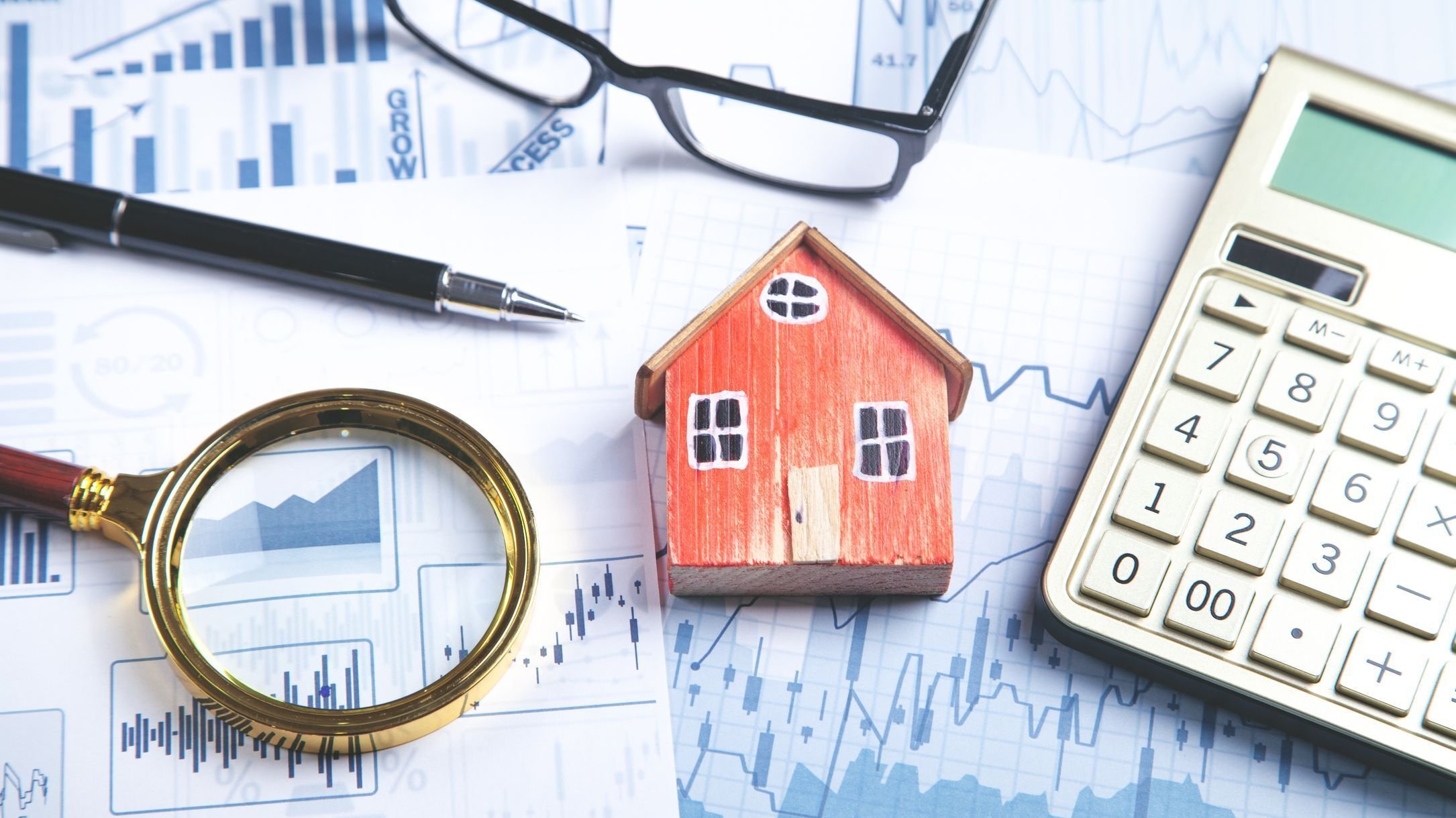House model, magnifying glass, eyeglasses, pen, calculator on the financial graphs.