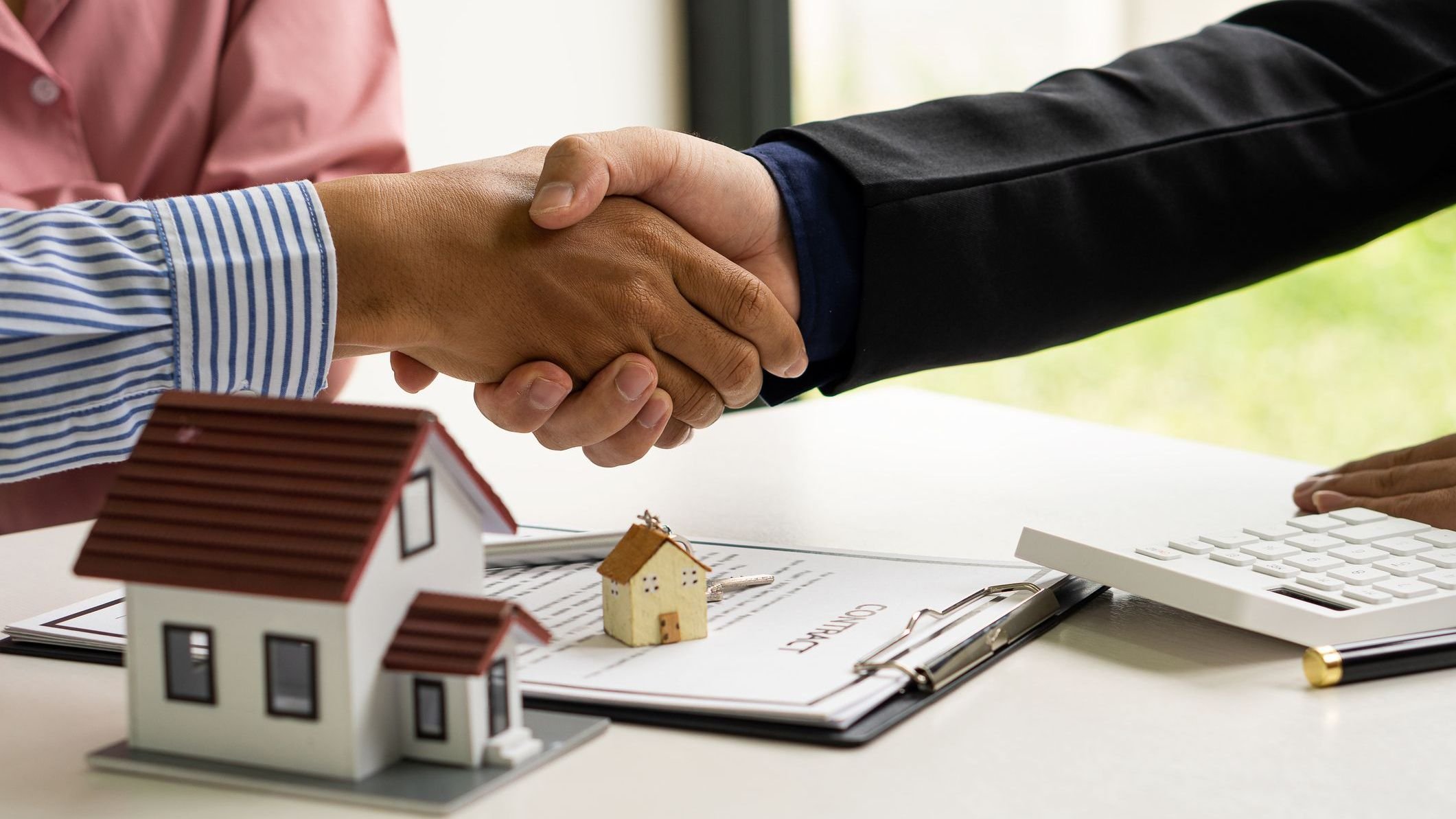 A handshake between the sales representative and the landlord when signing a home purchase or renting contact at the workspace desk. A real estate agent or bank officer explains the interest on a loan to customers with a home loan agreement and interest