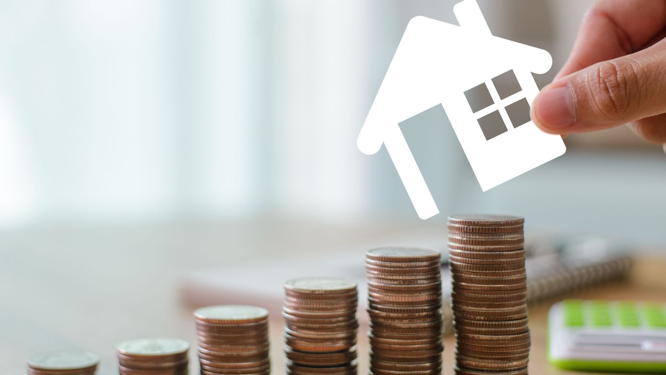 Close up image hand of young businesswoman holding a model of a white house and is about to place it on a money. Demonstrates saving money to buy a house or invest in real estate with calculator.