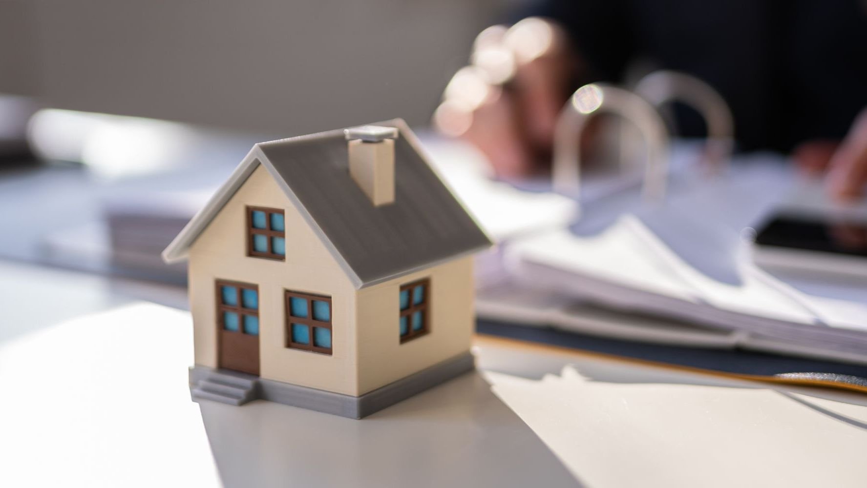 Small house sitting on table in front of man looking at papers.