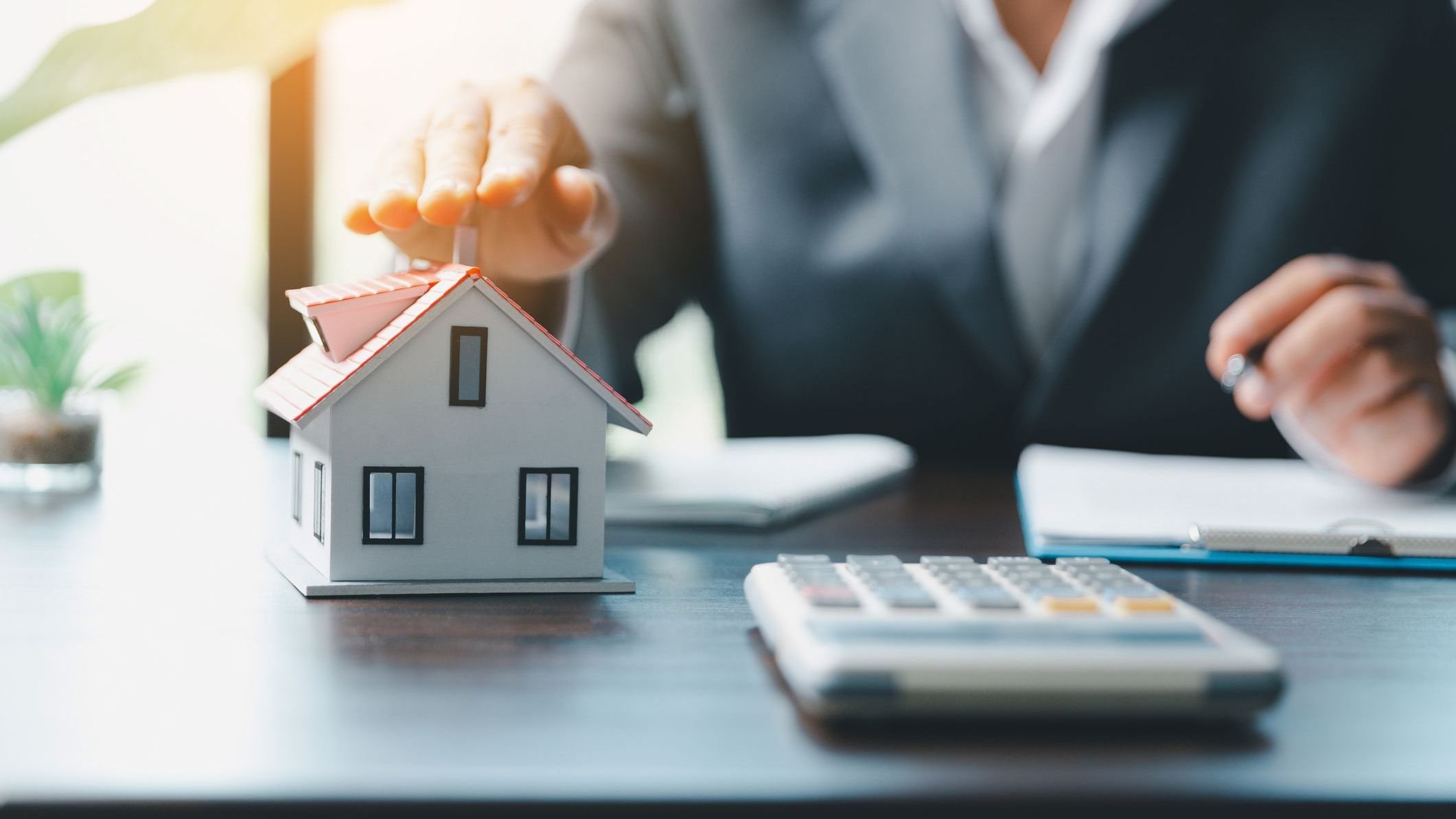 Female hands saving small house with a roof and a calculator sitting on the table.