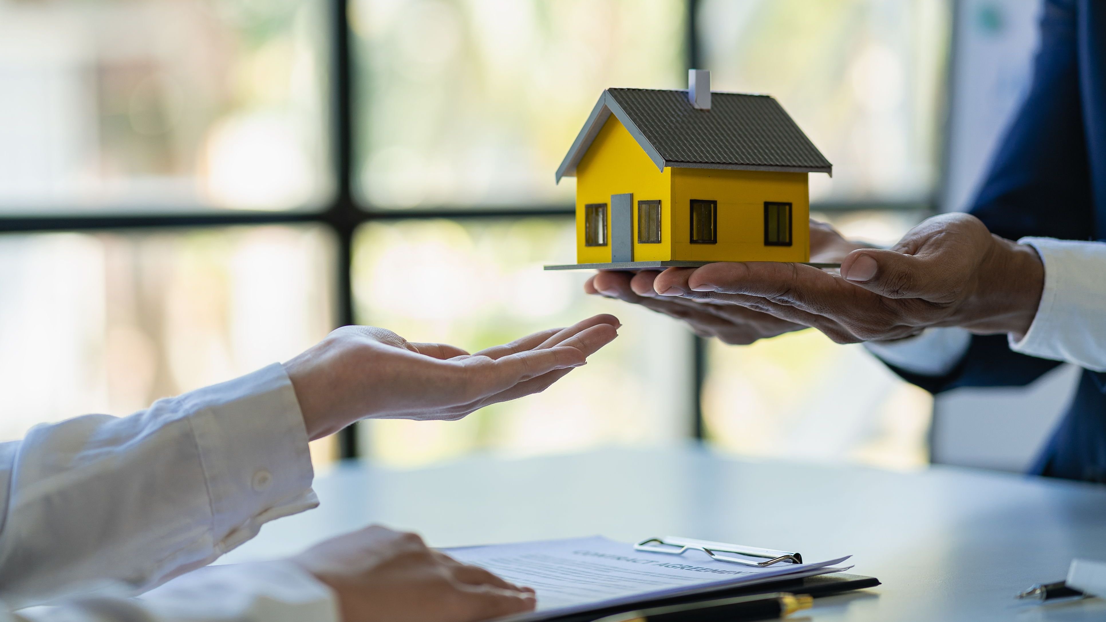 Person holding little house, other person signing papers.