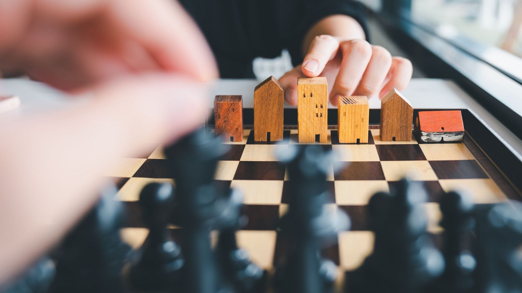 Hand of business man moving chess to Building and house models in chess game.