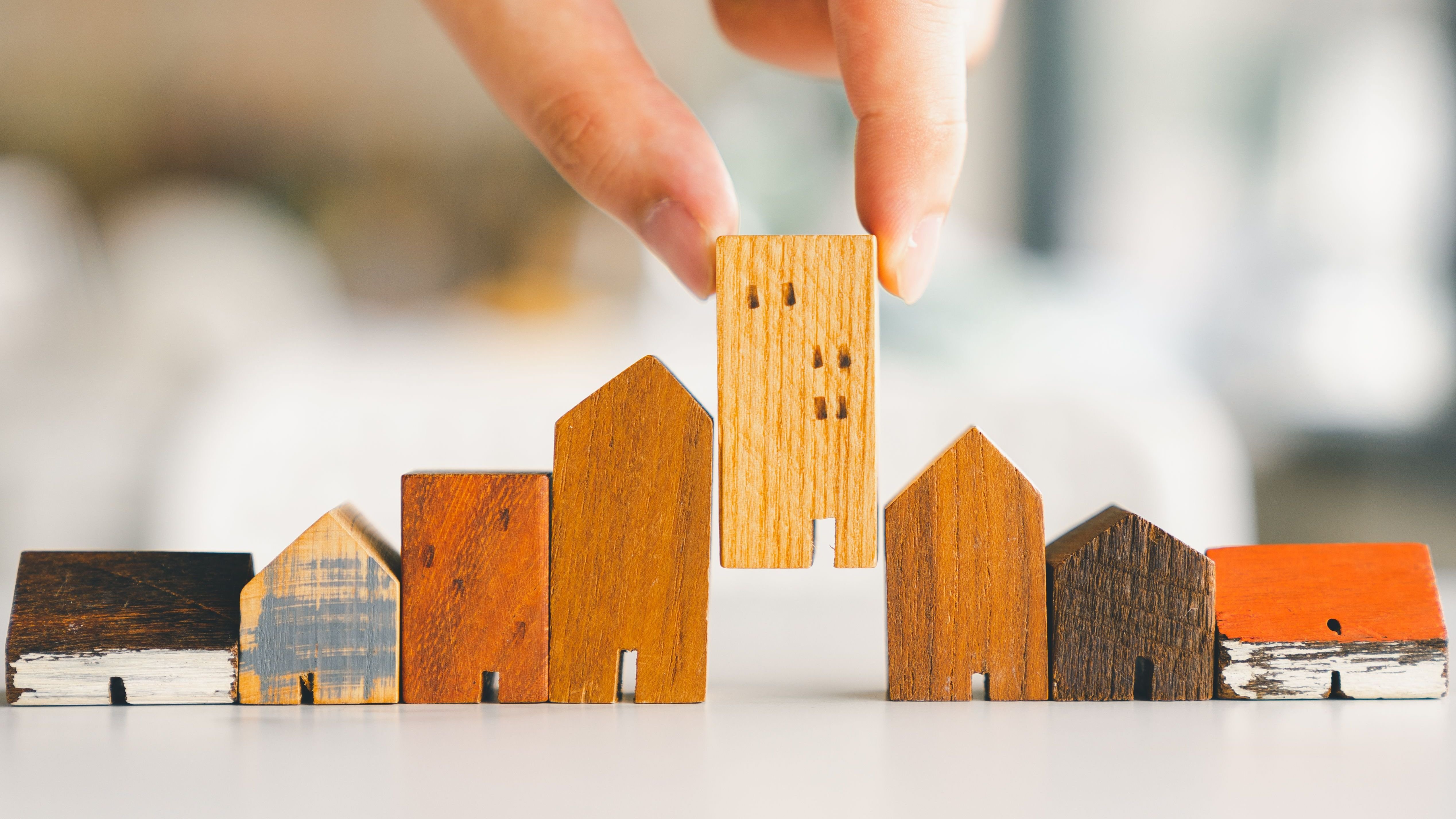 Hand choosing mini wood house model from model and row of coin money on wood table