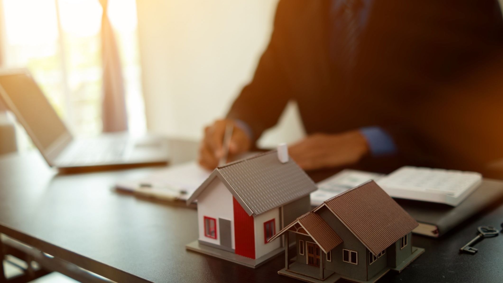 Real estate agent places miniature model home on desk inside real estate sales office.