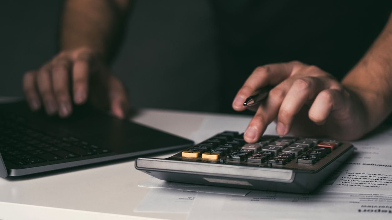 Man is using a calculator to calculate his monthly miscellaneous expenses at home.