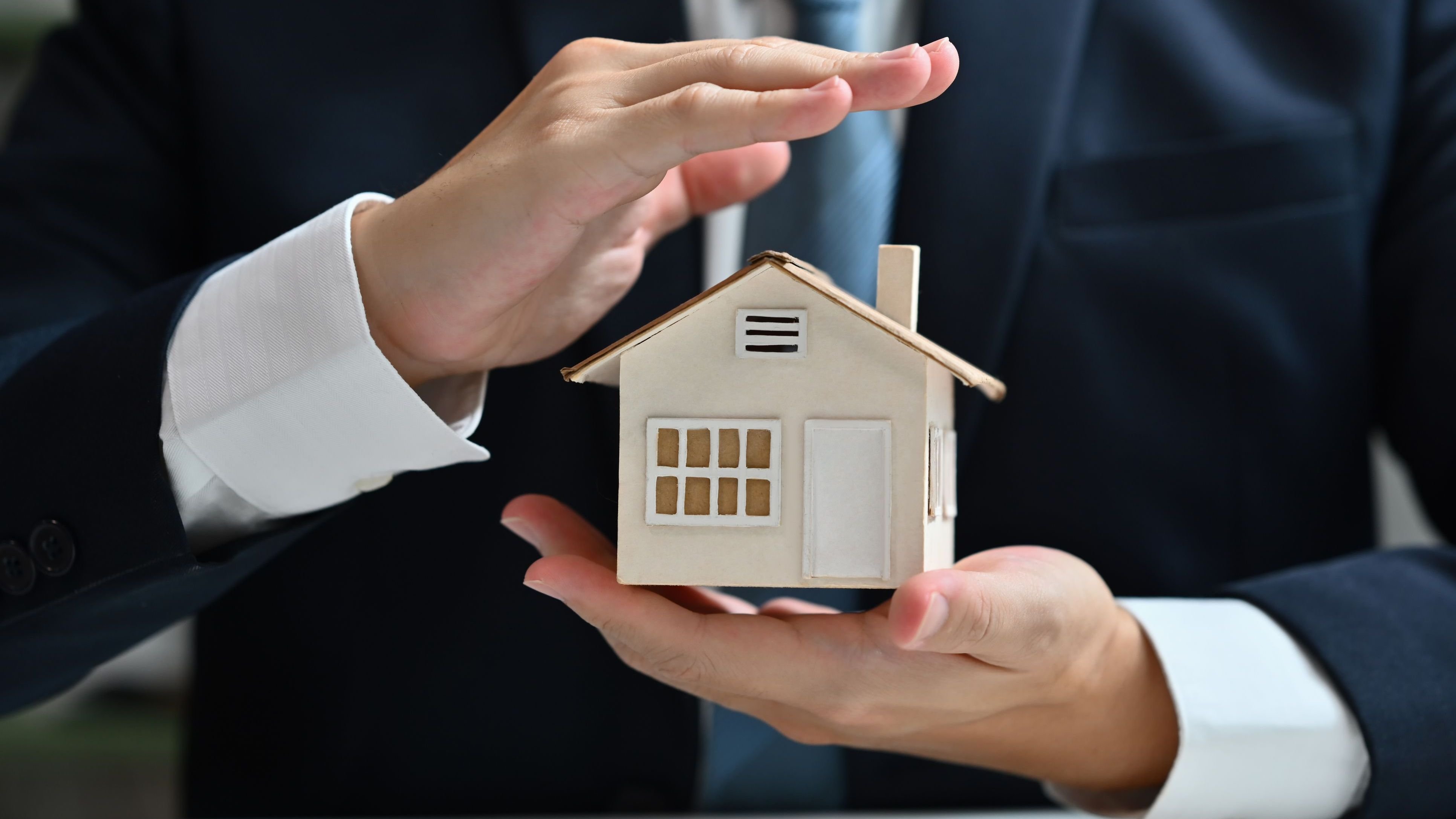 Businessman protecting house model with hands.