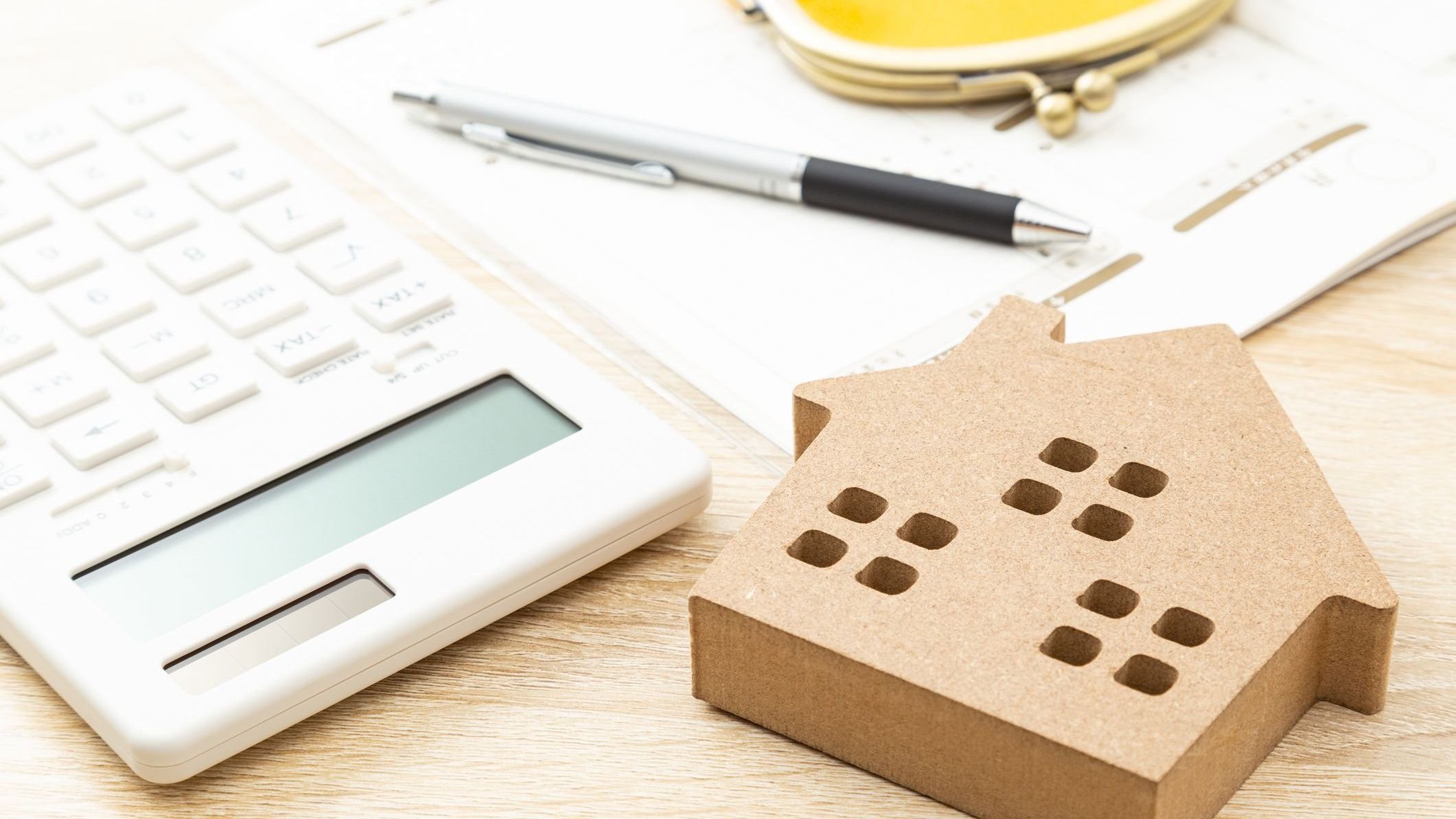 Wooden house, calculator, and stack of papers with a pen sitting on top.