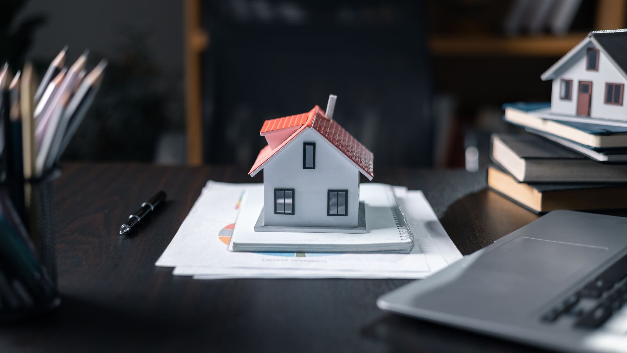 Model house, paperwork and cash money on a desktop.