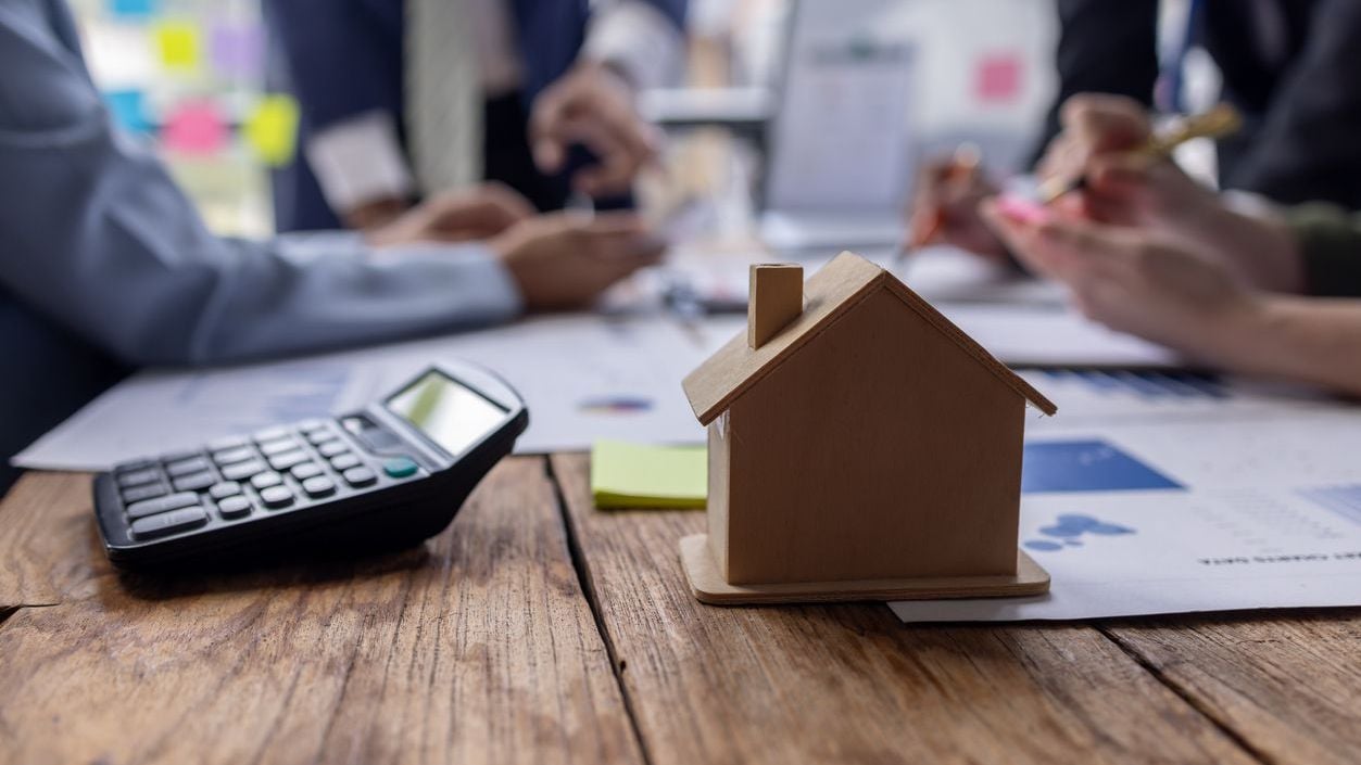 Businessman holding model small building house with property insurance at table.