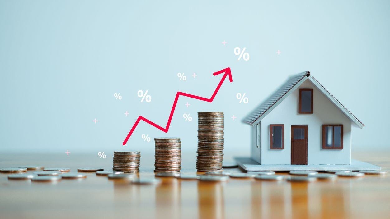 Stack of coins with upwards arrow and, percent signs next to small house.