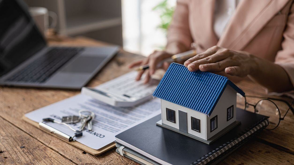 Little house, stack of papers and a person using a calculator.