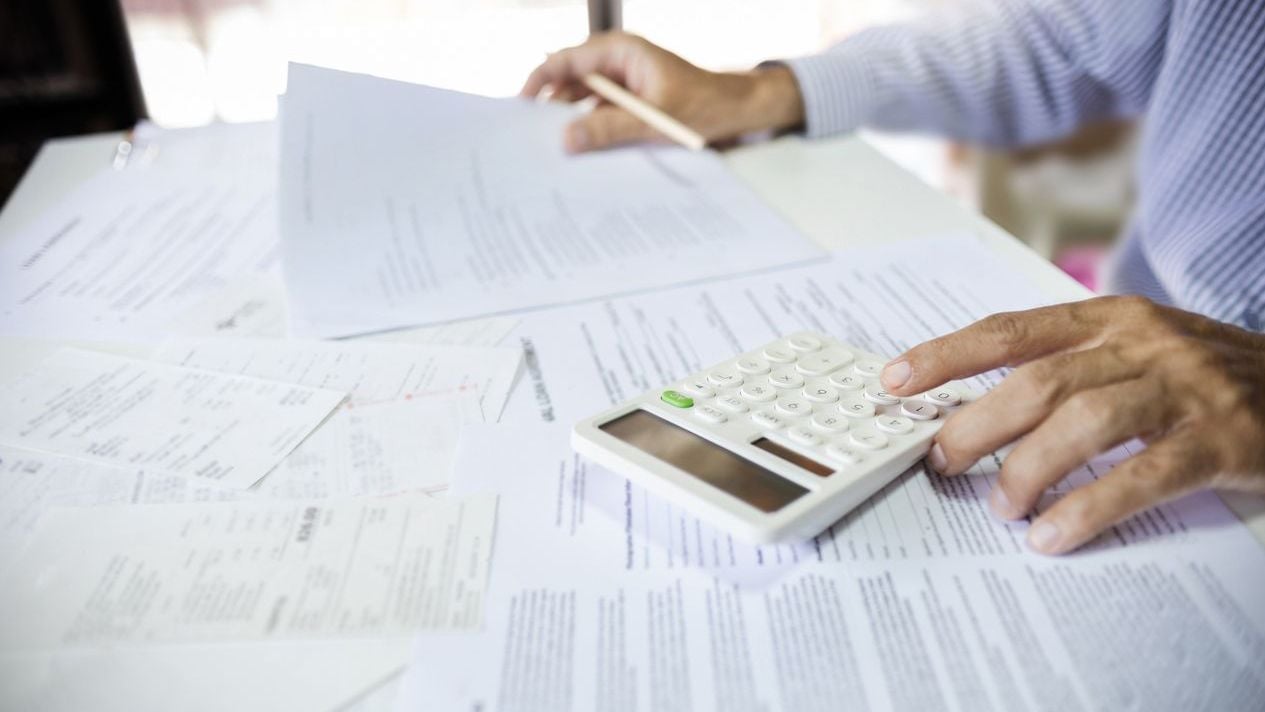 Stack of business papers sitting on desk with calculator.