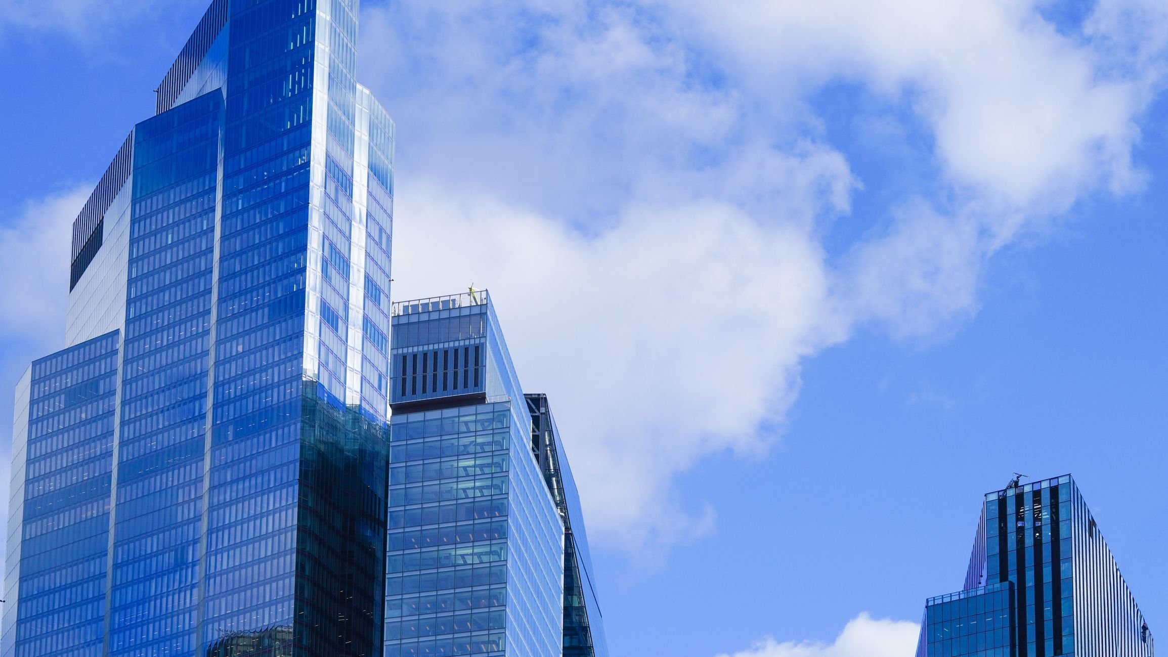 Towering blue glass skyscraper reflecting sky and city buildings.