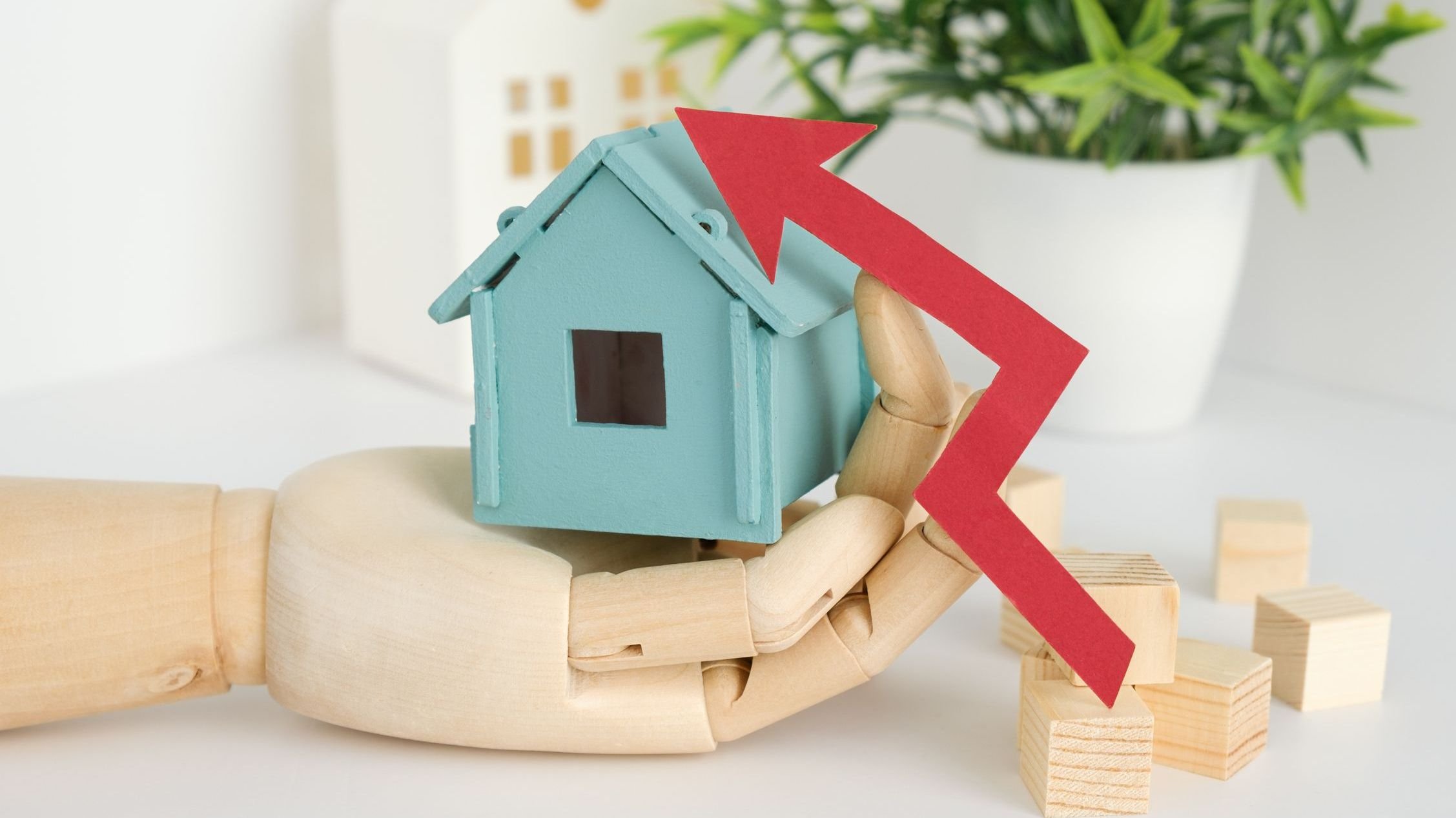 A hand holding a blue house with a red arrow pointing upwards.