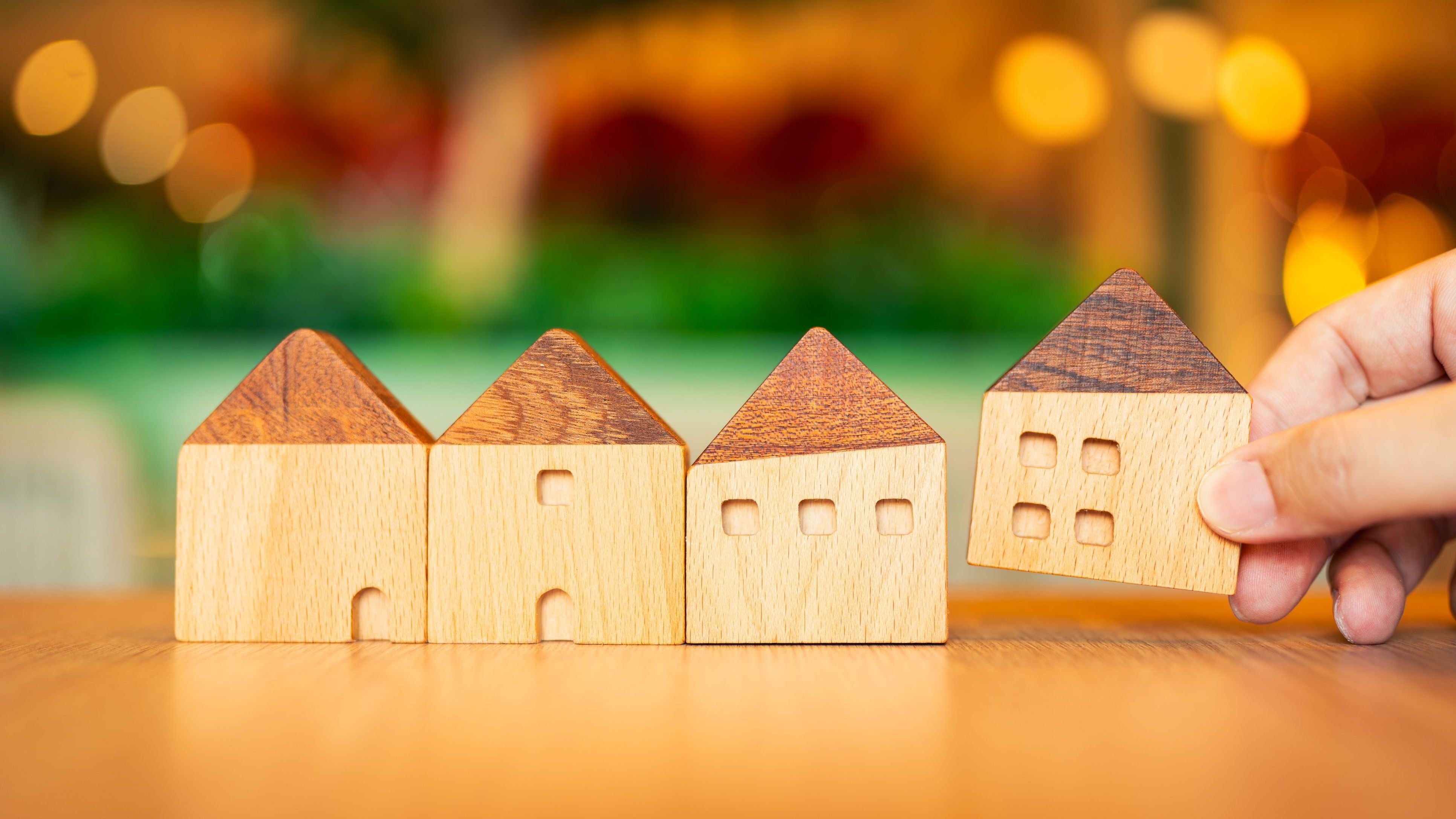 Hand choosing mini wood house model from model on wood table, selective focus.