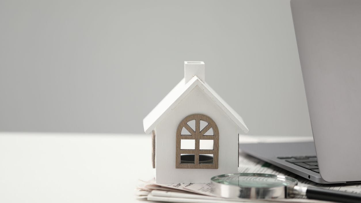 Papers, magnifying glass, laptop and house figure on white table.
