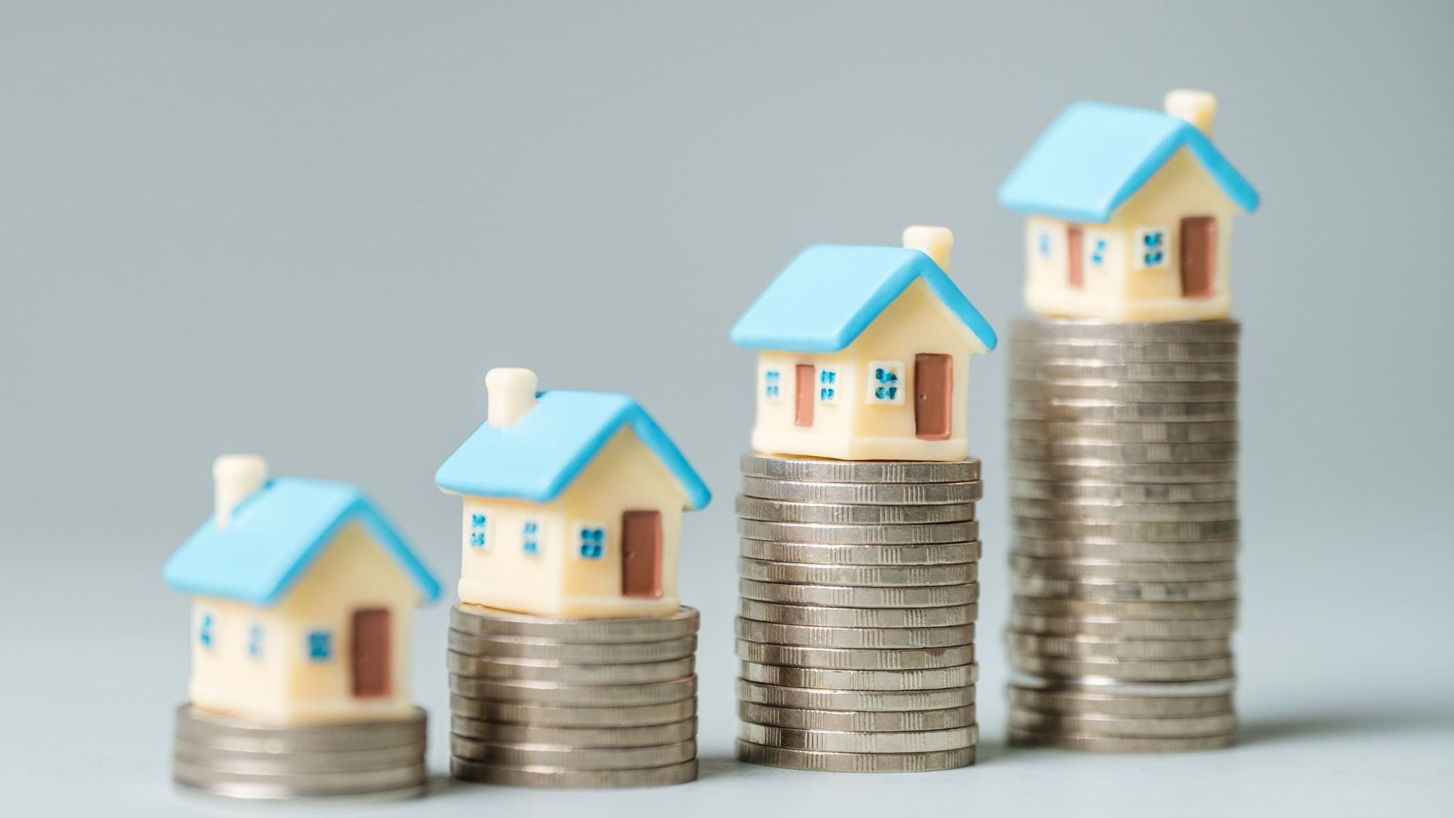 A stack of coins and a house model are shown in a row.