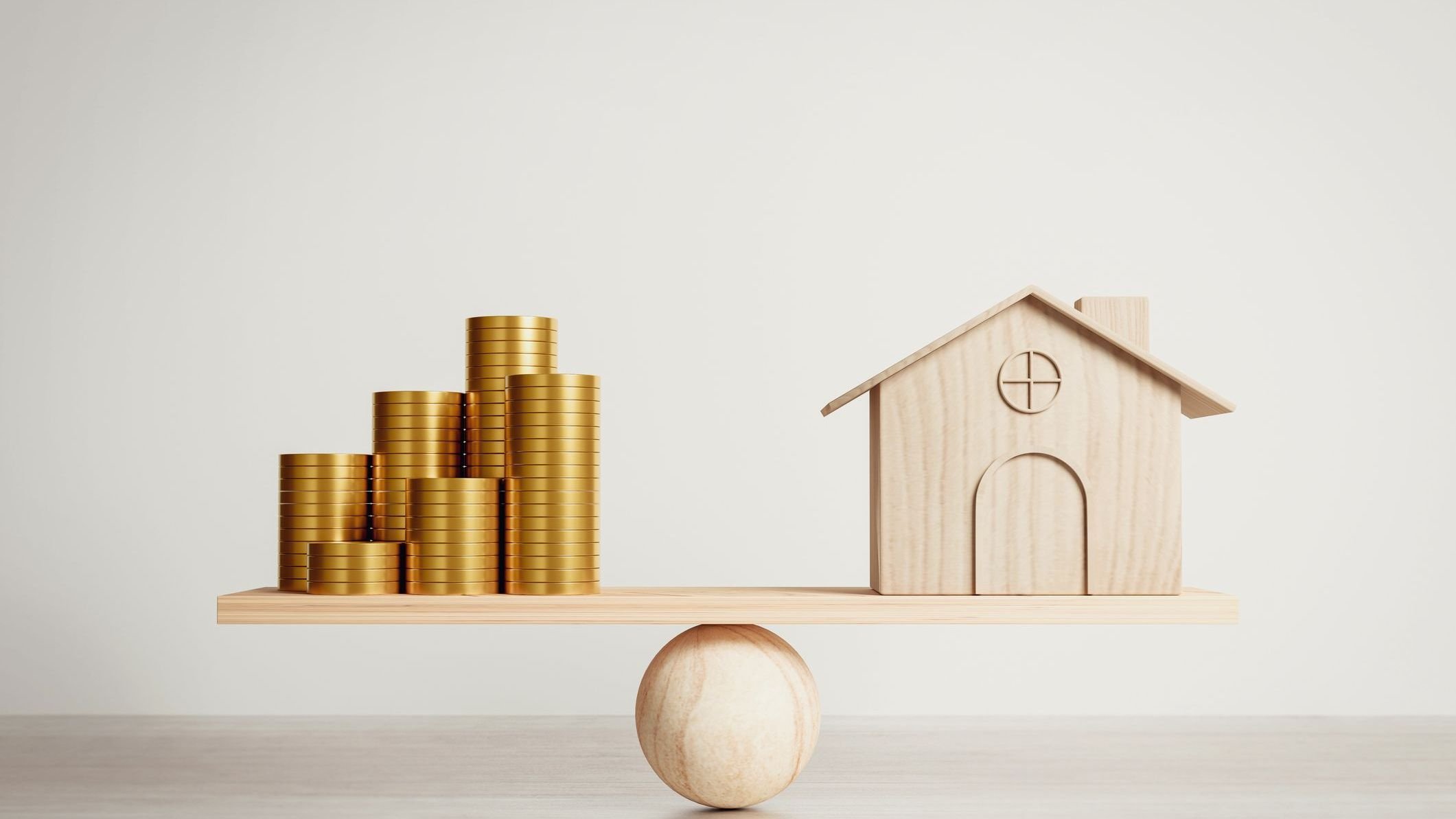 Small wooden house and gold coins on a wooden scale.