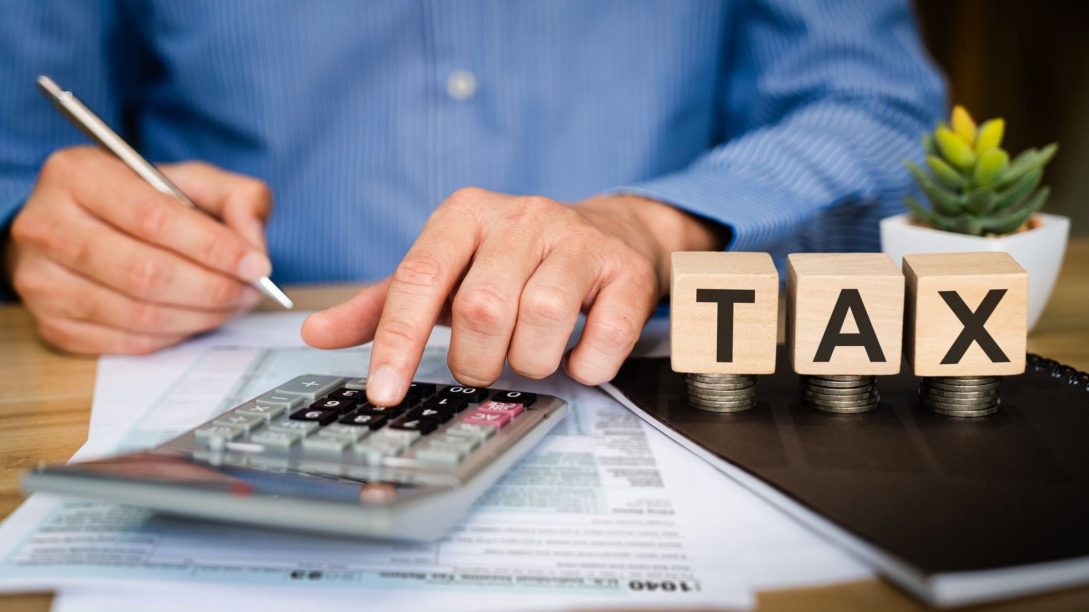 Business professional calculating tax with calculator and pen on financial documents, wooden TAX blocks on desk.