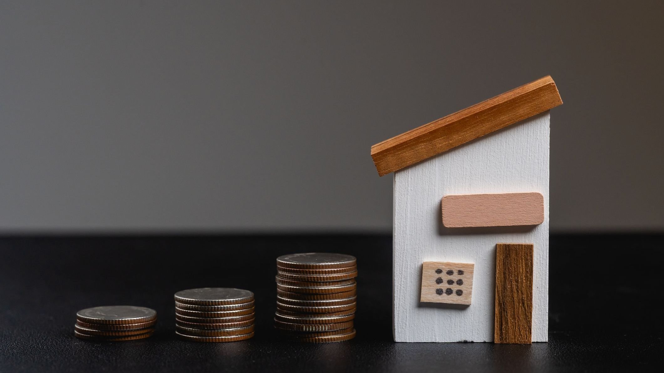 Small wooden house model next to stacks of coins representing financial growth, investment in real estate, and savings concept for home ownership.