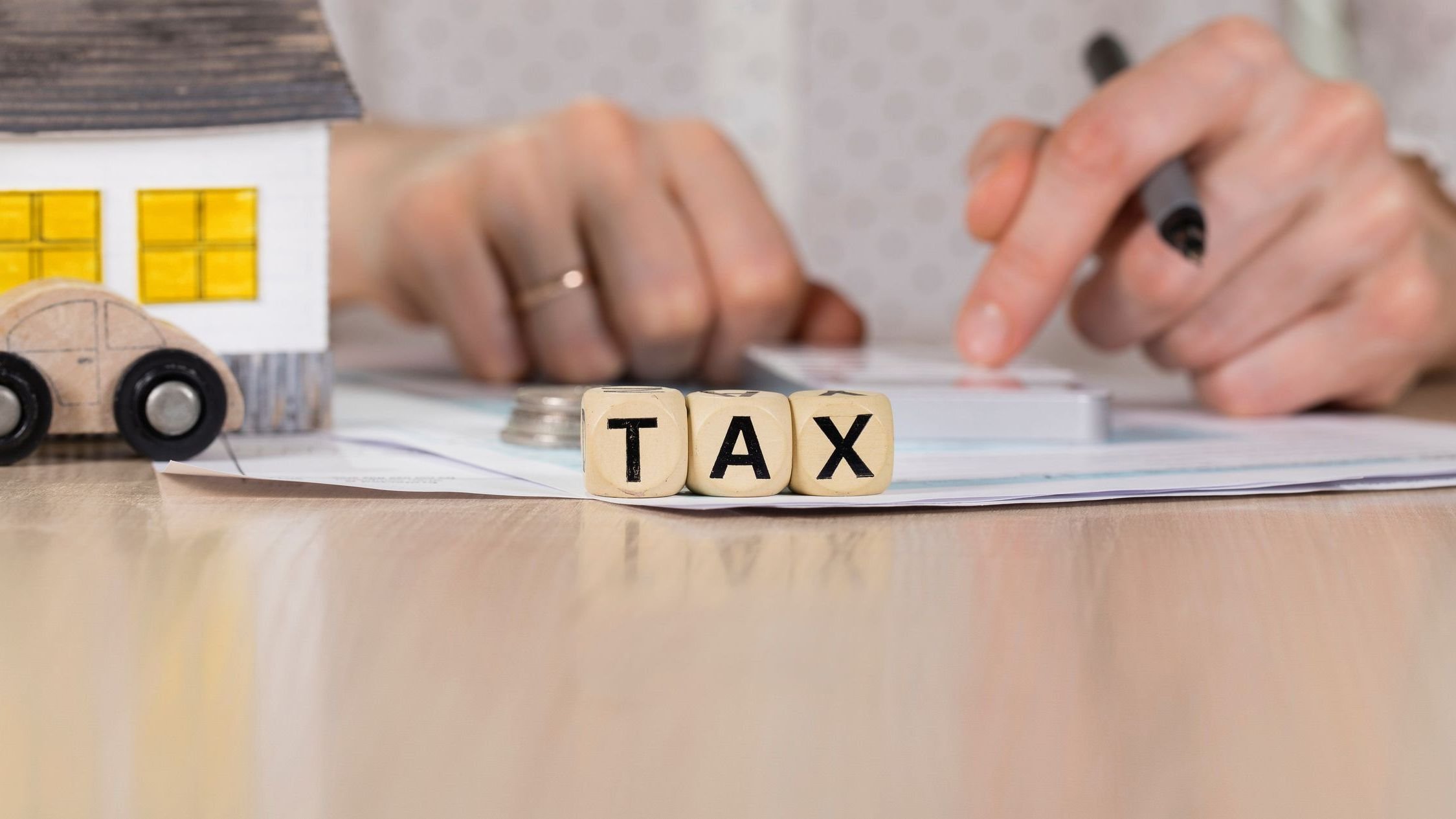 Word TAX composed of wooden letters. Female hand with a pen in the background.