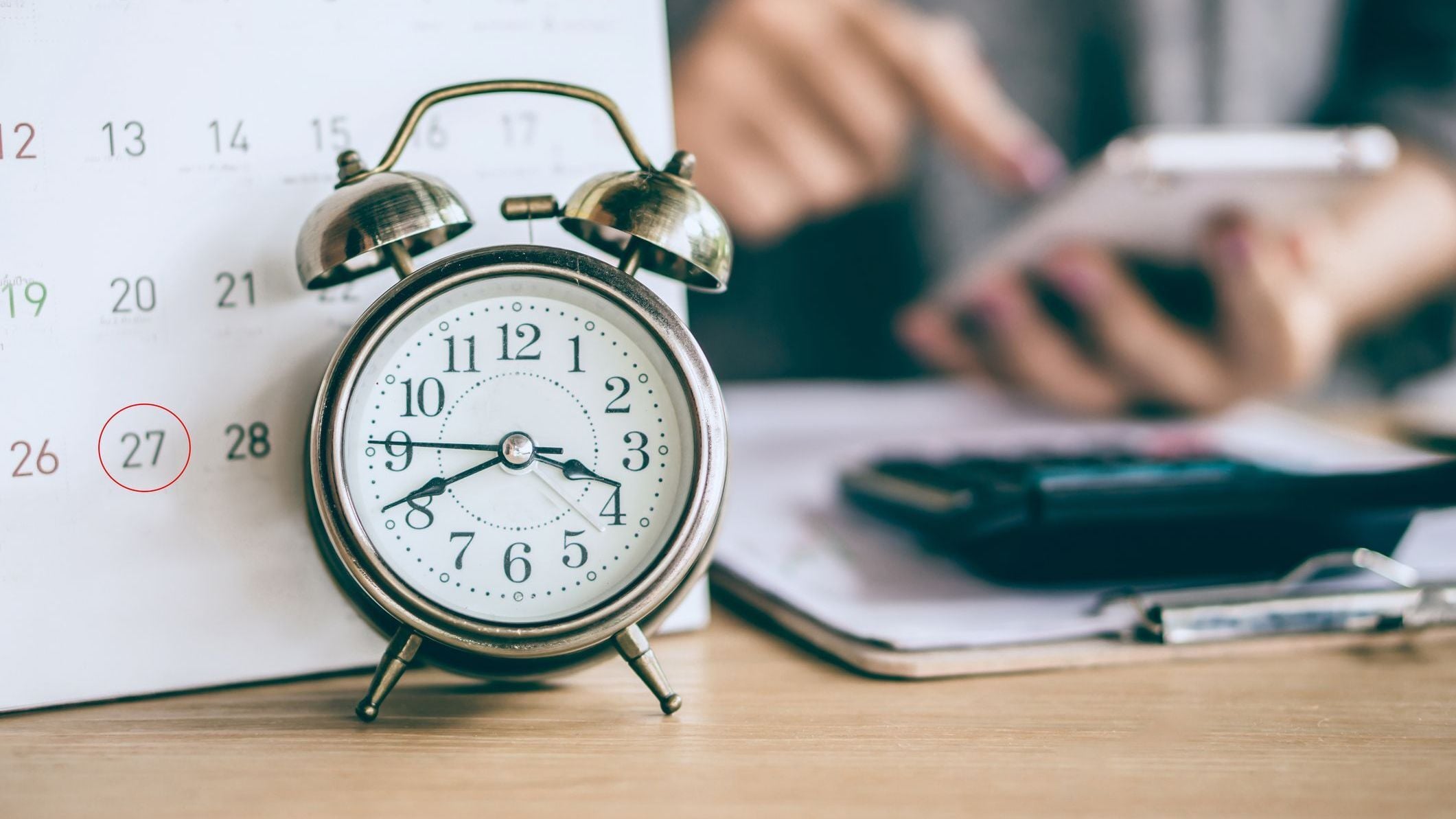 Due date calendar and alarm clock with blur business woman hand calculating 
