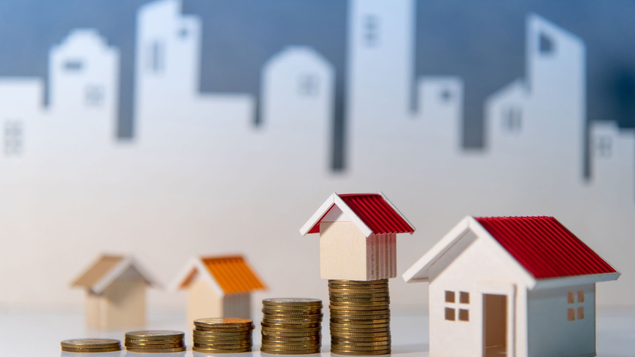 Coins stack and house model on the table with white city background. 
