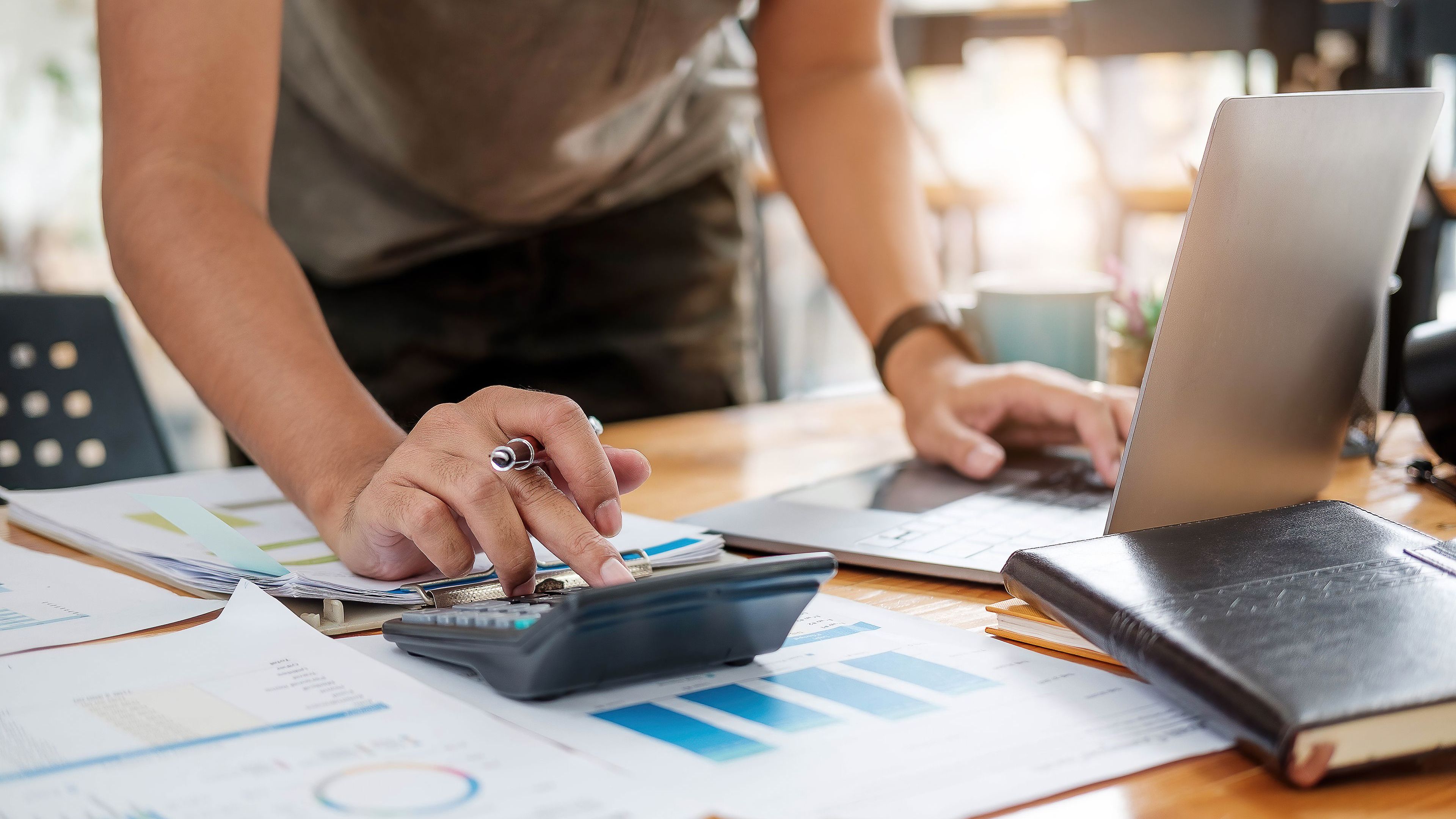 Close up of businessman or accountant hand holding pen working on calculator.