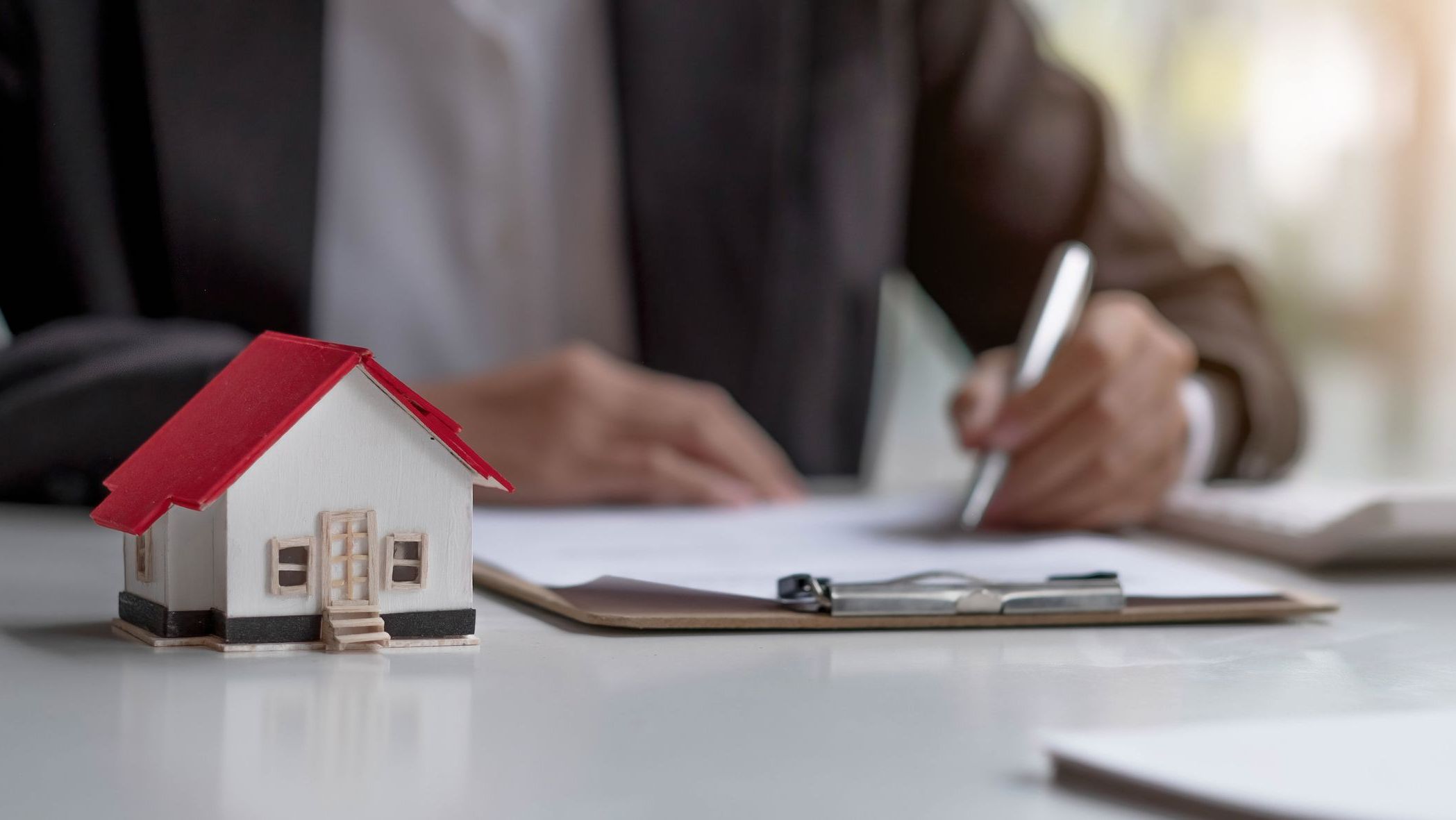 Real estate agents work at desks in rooms with paperwork and house designs to introduce clients.