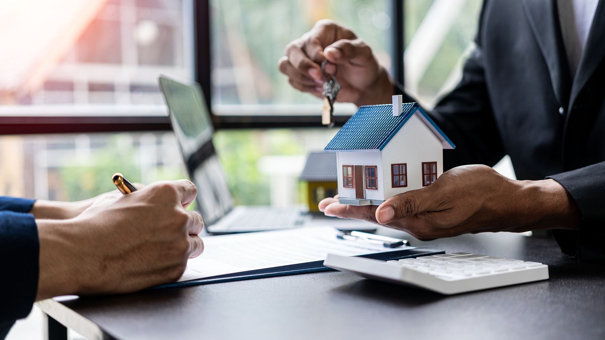 Real estate agents offer contracts to buy or rent housing. Businessman holding model small building house with property insurance at table in home sales office.