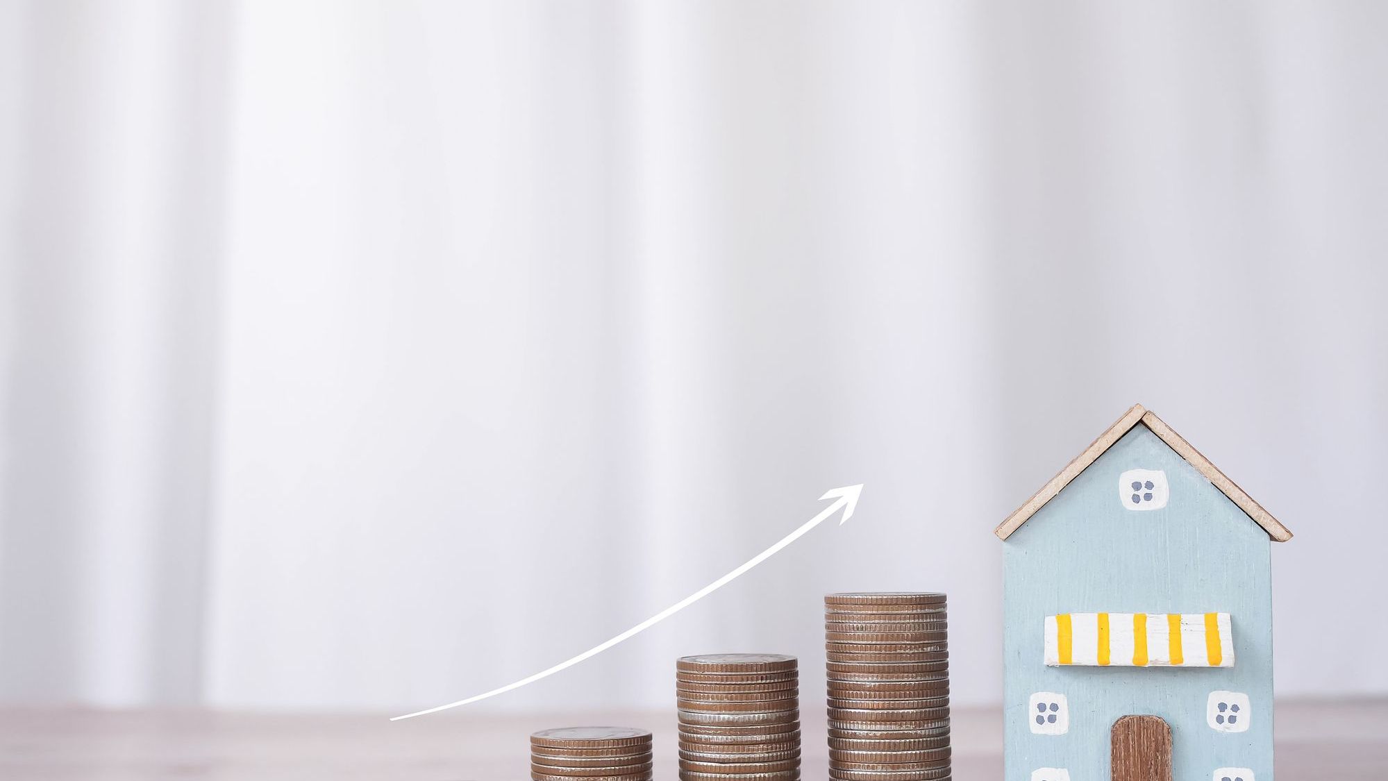 Miniature house and stack of coins with arrow rising. 