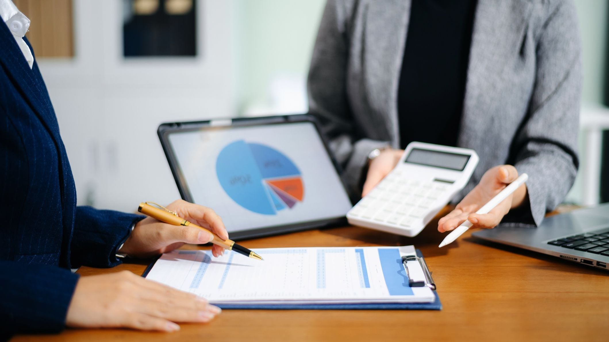 Two businesswomen review cash flow forecast and business growth charts on tablet and clipboard in office. Finance, data analytics, and planning concept for professionals.