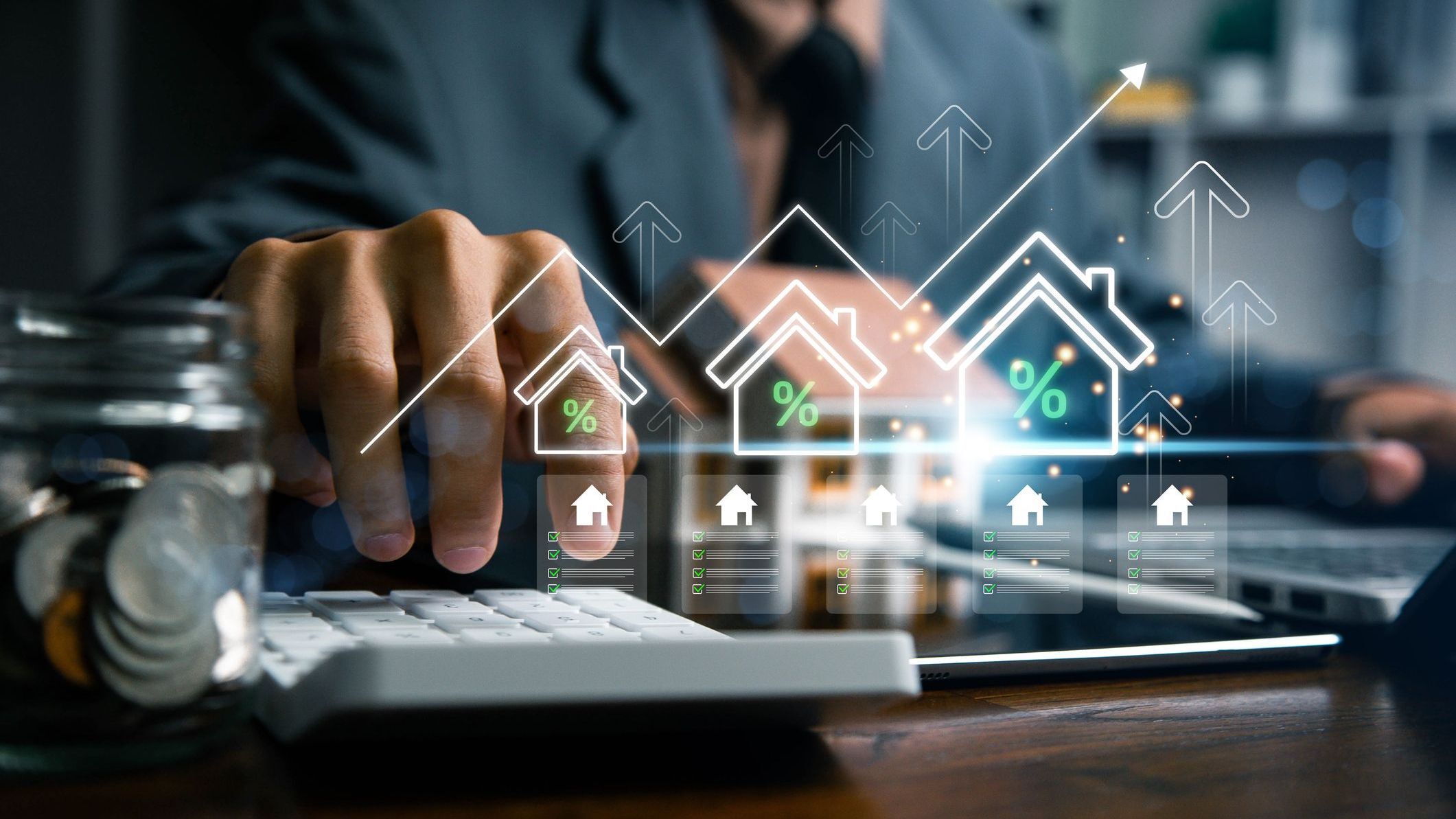 Real estate investment and mortgage calculation concept with businessman using calculator, coins stacked on desk, laptop, and small house model.