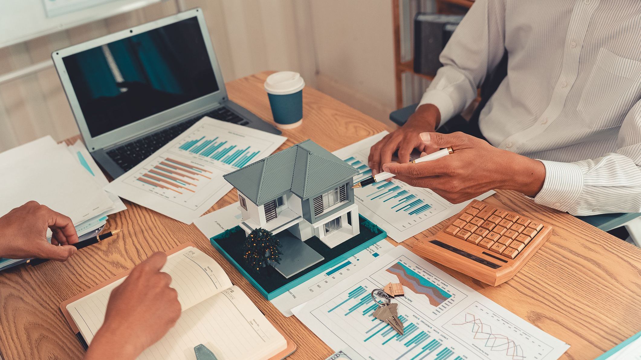 Real estate agent explaining housing details and loan conditions to client with house model on desk. 